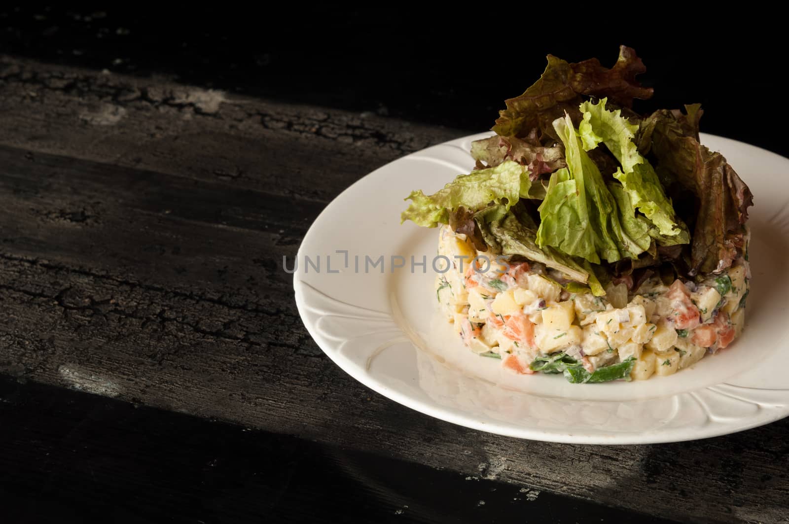 salad olivier in a white plate on a wooden old surface. Olivier salad with greens in a round plate on a wooden old board