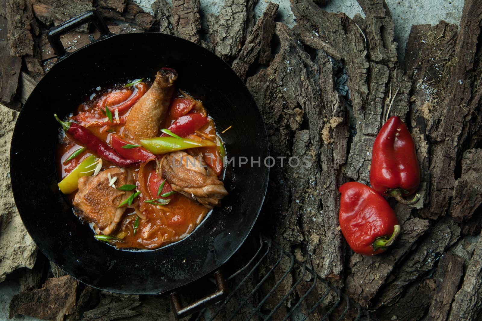 chicken dish with vegetables in a frying pan on the background of tree bark