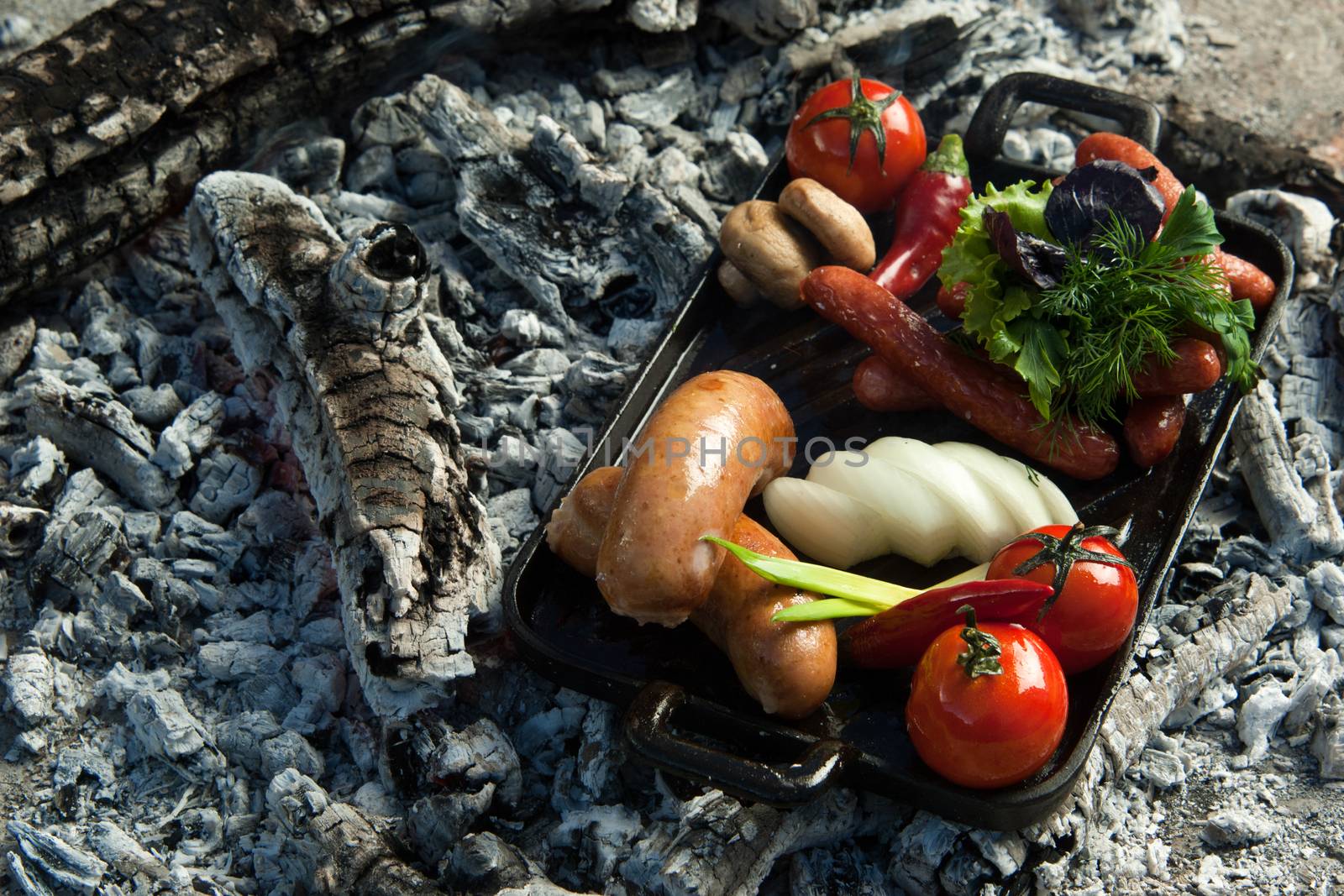 smoked sausages and tomatoes lie on charcoal. the dish is cooked and smoked on charcoal