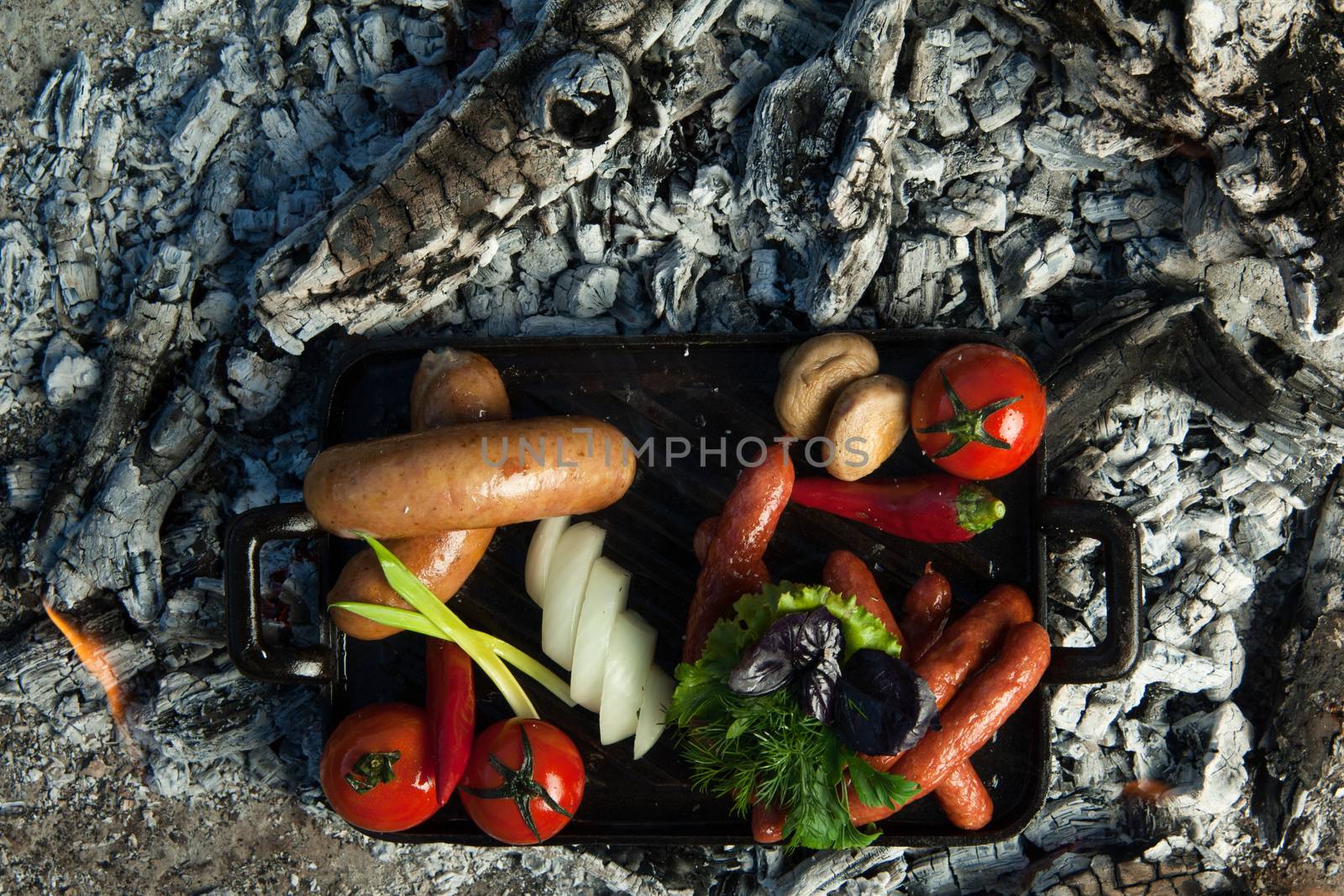 smoked sausages and tomatoes lie on charcoal. the dish is cooked and smoked on charcoal