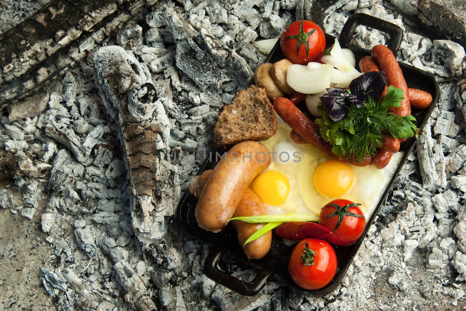 smoked sausages with tomatoes and eggs lie on charcoal. the dish is cooked and smoked on charcoal