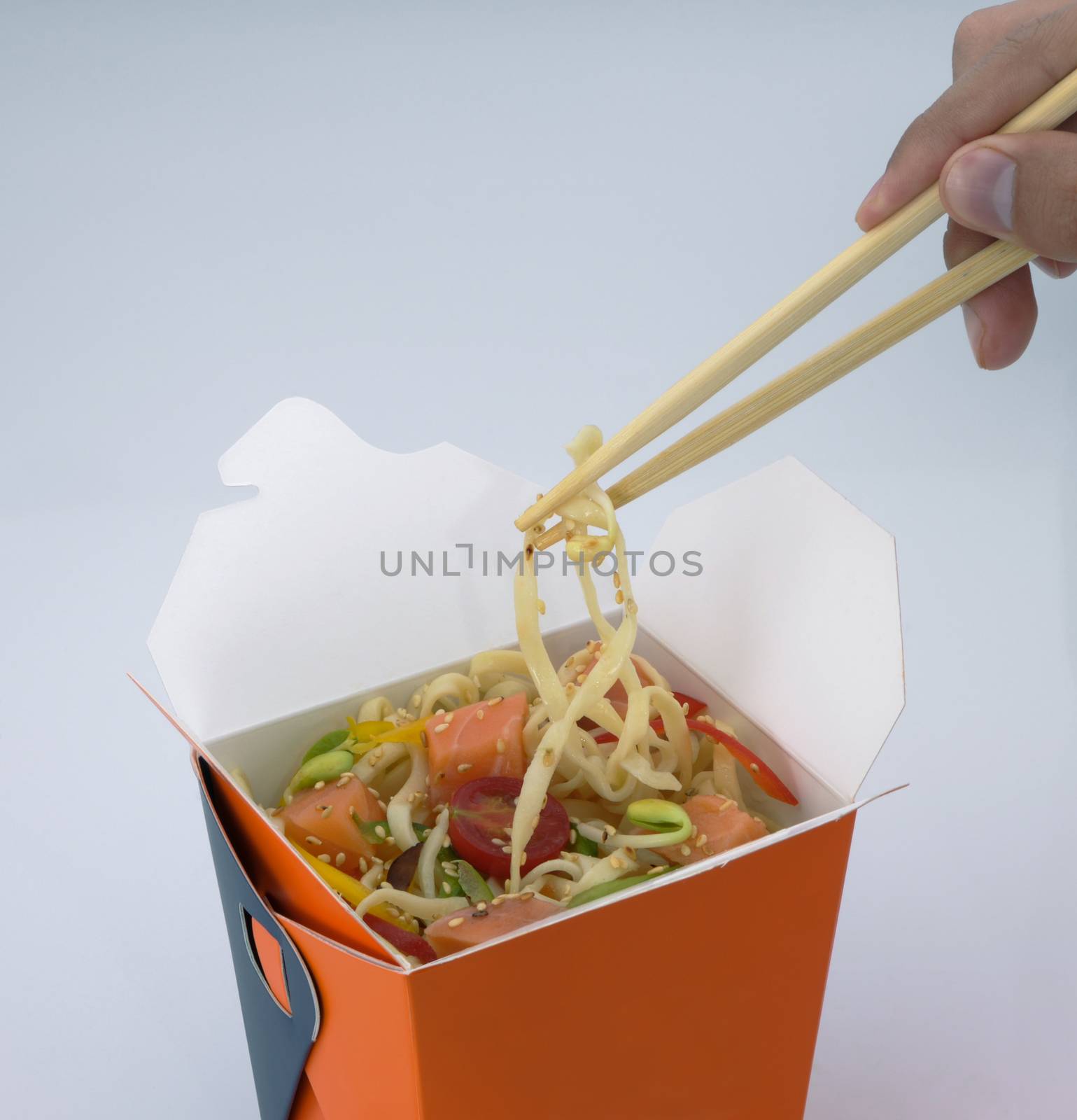 chinese food to takeaway. noodles with meat and vegetables in a cardboard box on a light background. takes chinese food with chopsticks