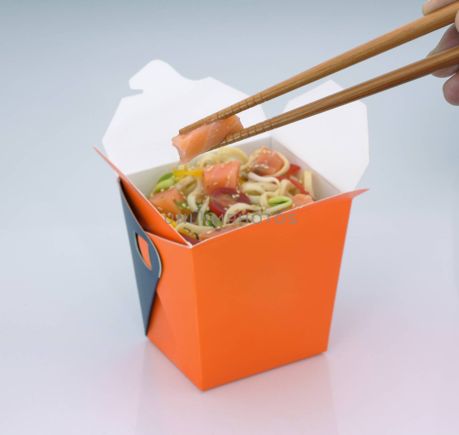 chinese food to takeaway. noodles with meat and vegetables in a cardboard box on a light background. takes chinese food with chopsticks