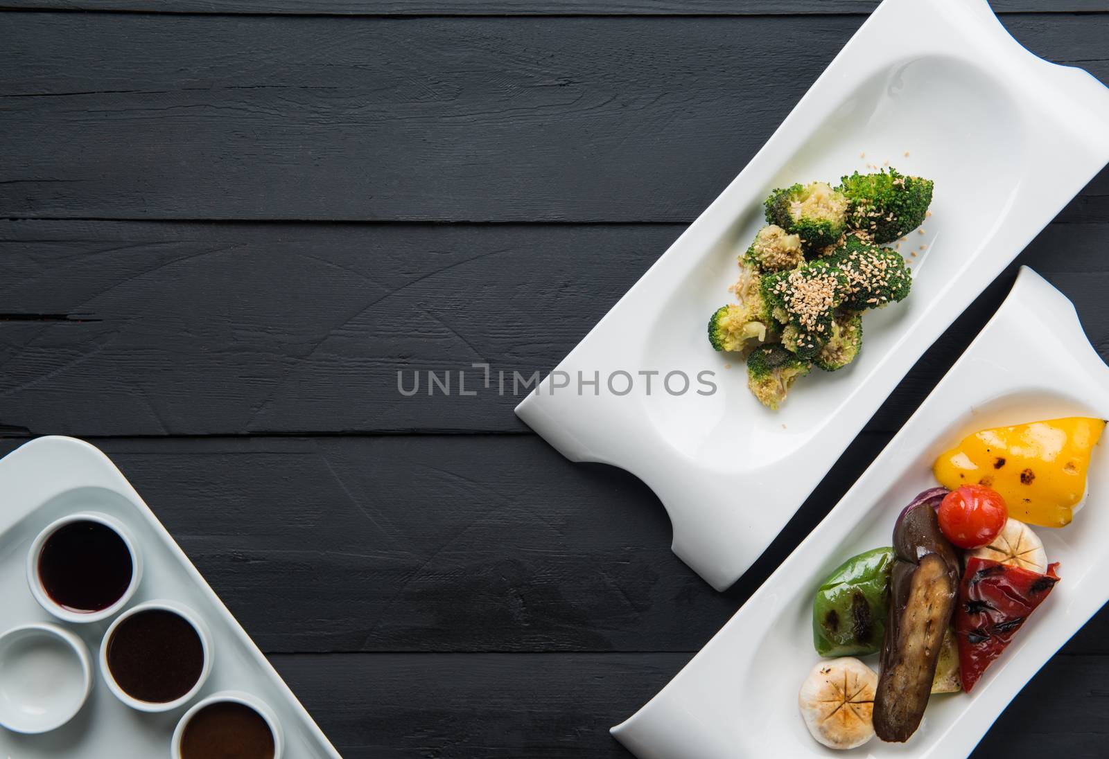 salads, vegetable food and sauces in plates on a black wooden background