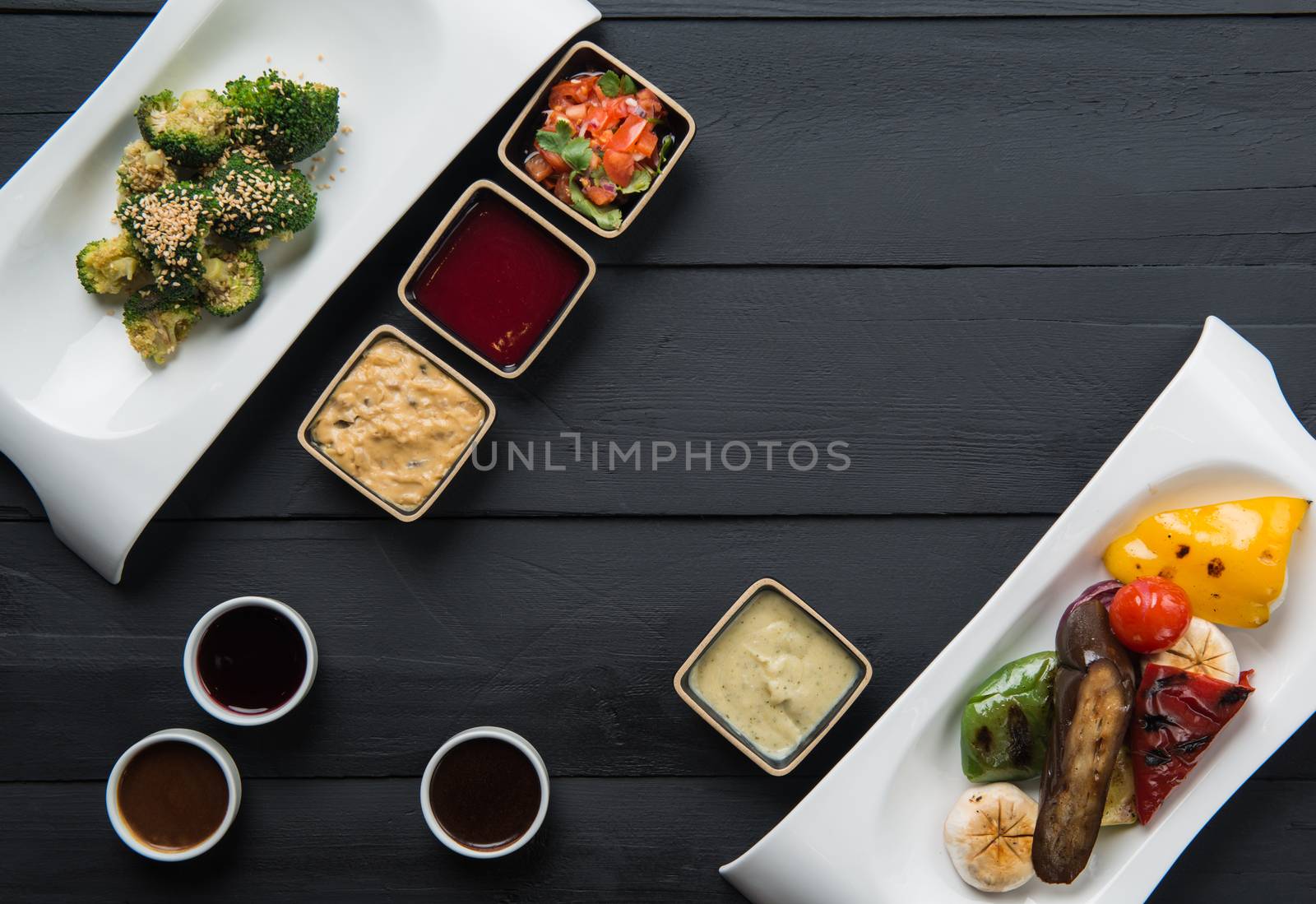 salads, vegetable food and sauces in plates on a black wooden background