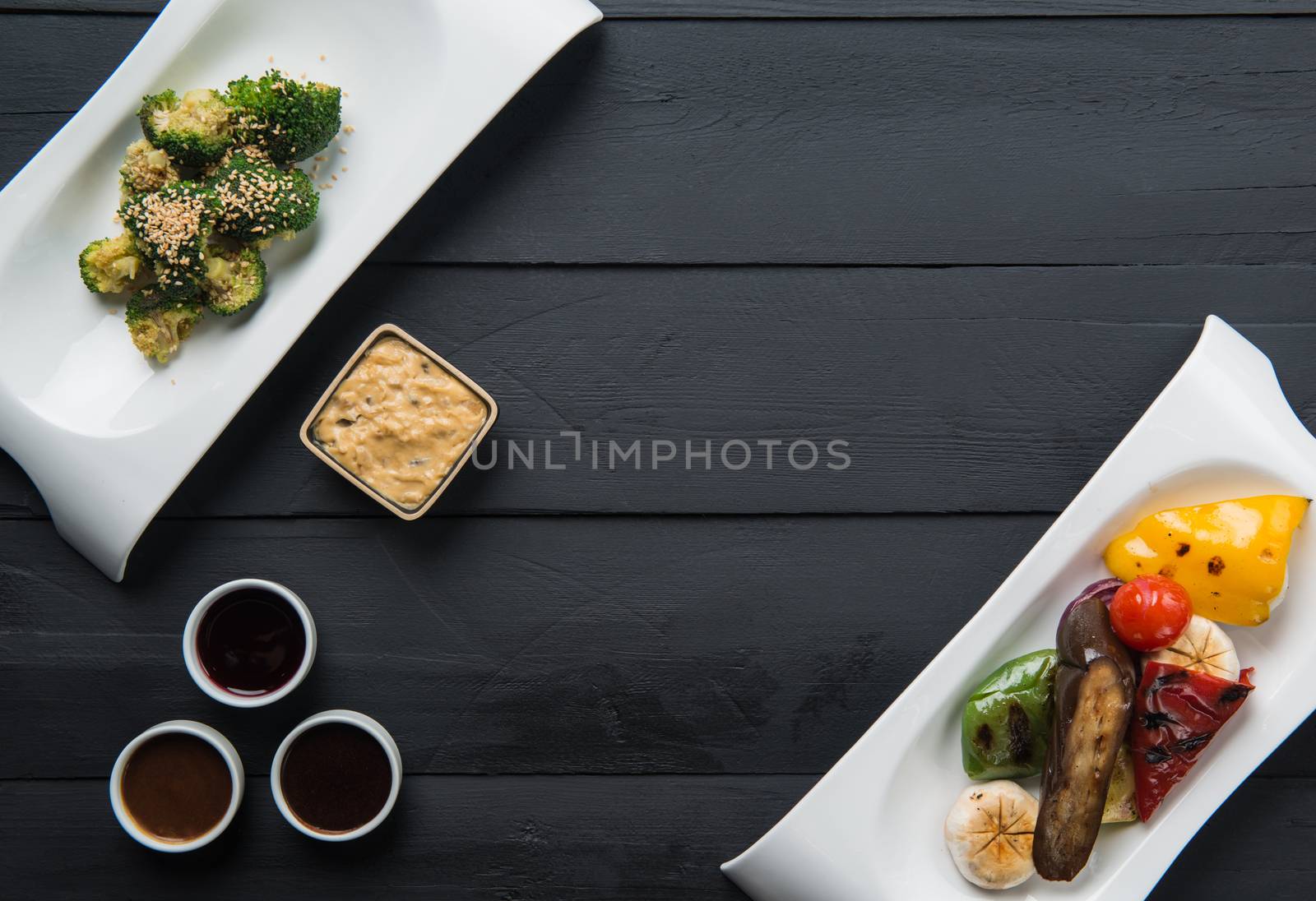 salads, vegetable food and sauces in plates on a black wooden background