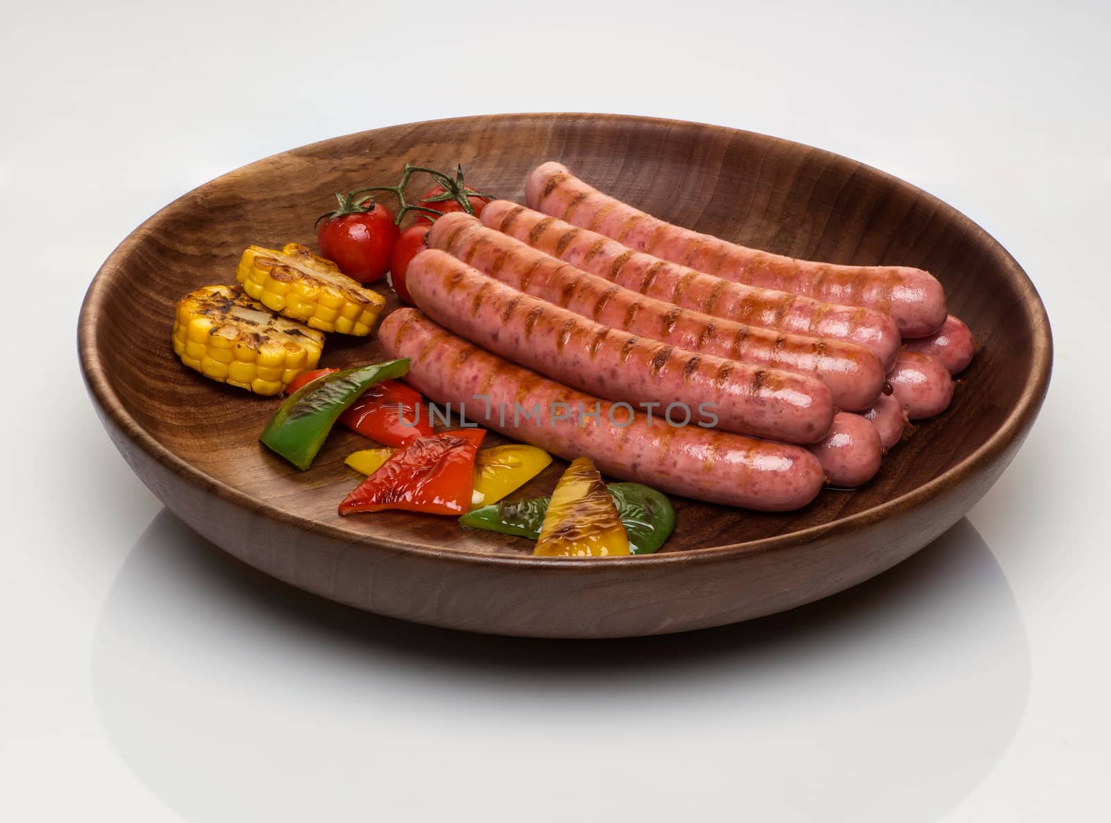 fried sausages with vegetables in a wooden plate, isolated on a white background