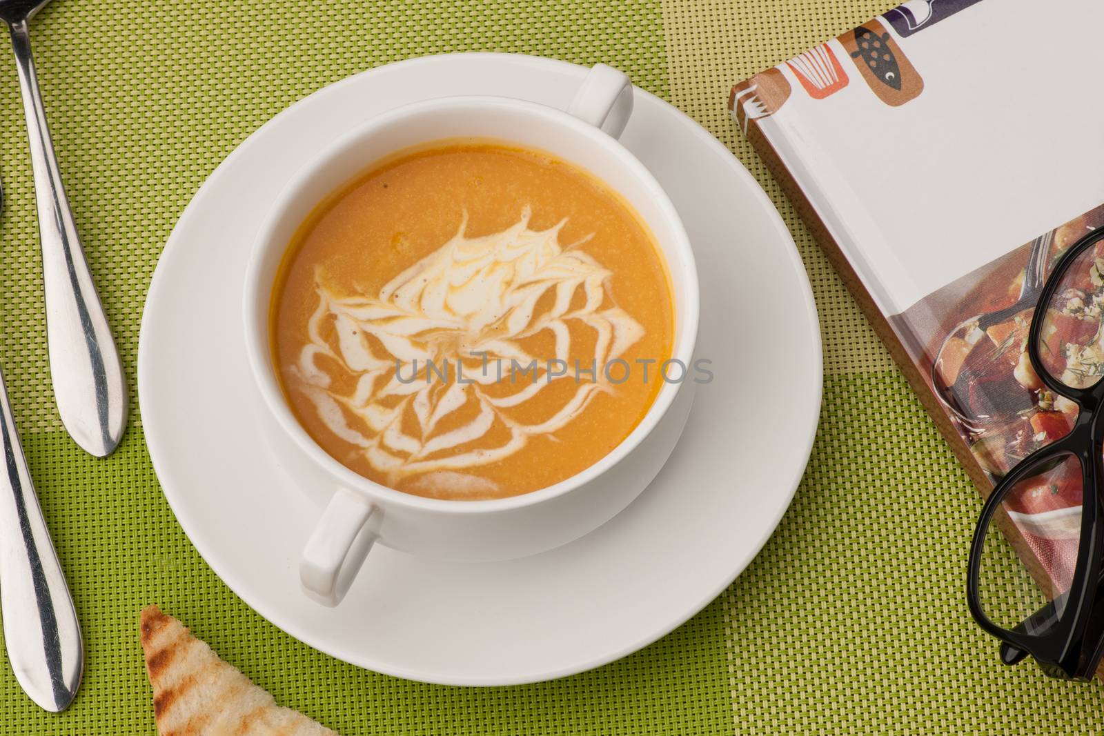 soup in a white bowl with book and glasses on a green tablecloth