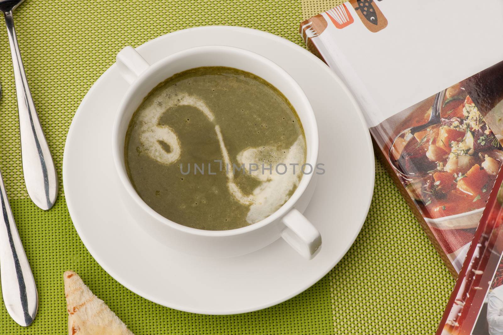 soup in a white bowl with a book and cutlery on a green tablecloth