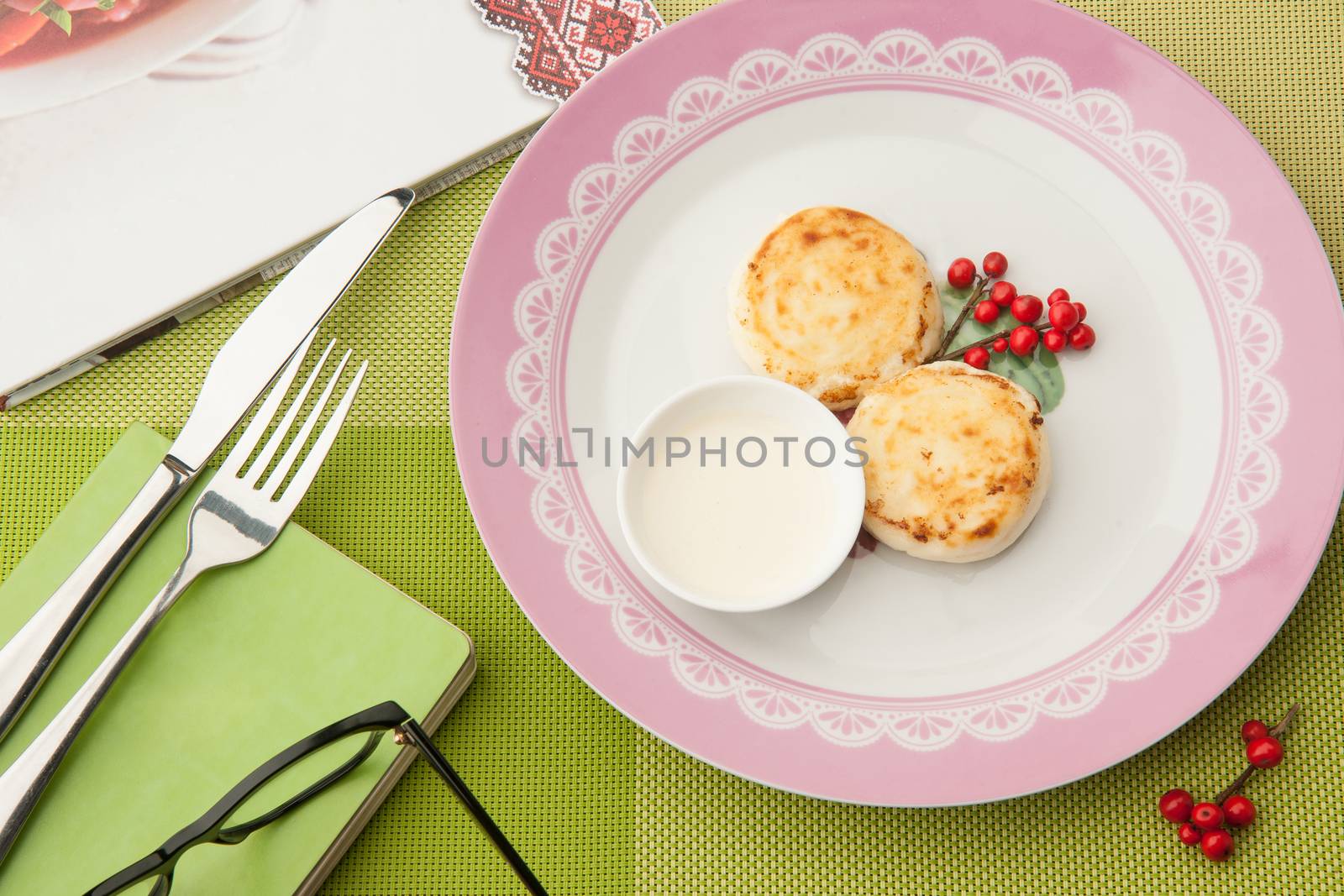 breakfast with berries on the plate with book and glasses and cutlery on a green tablecloth