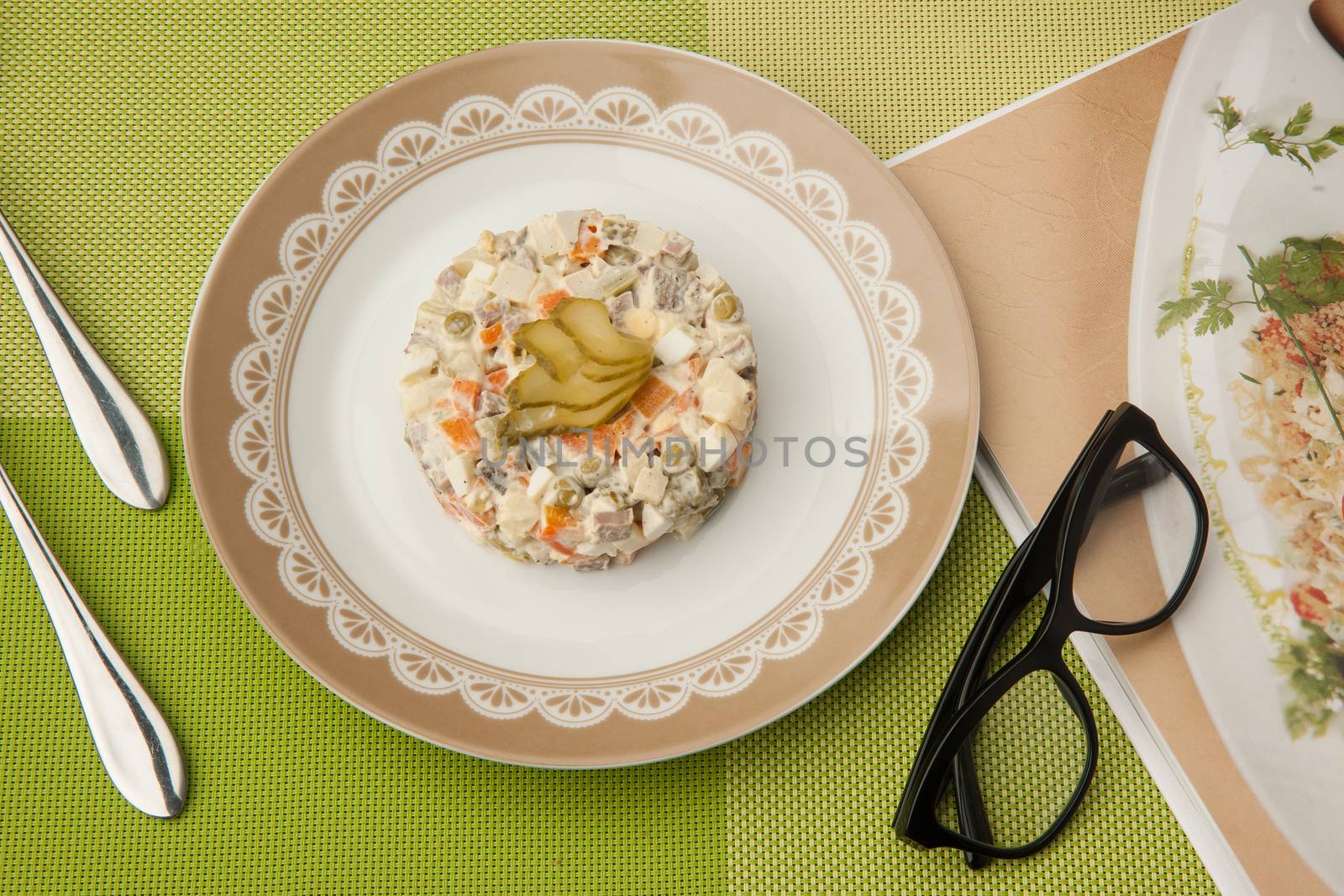 salad in a plate with book and glasses and cutlery on a green tablecloth