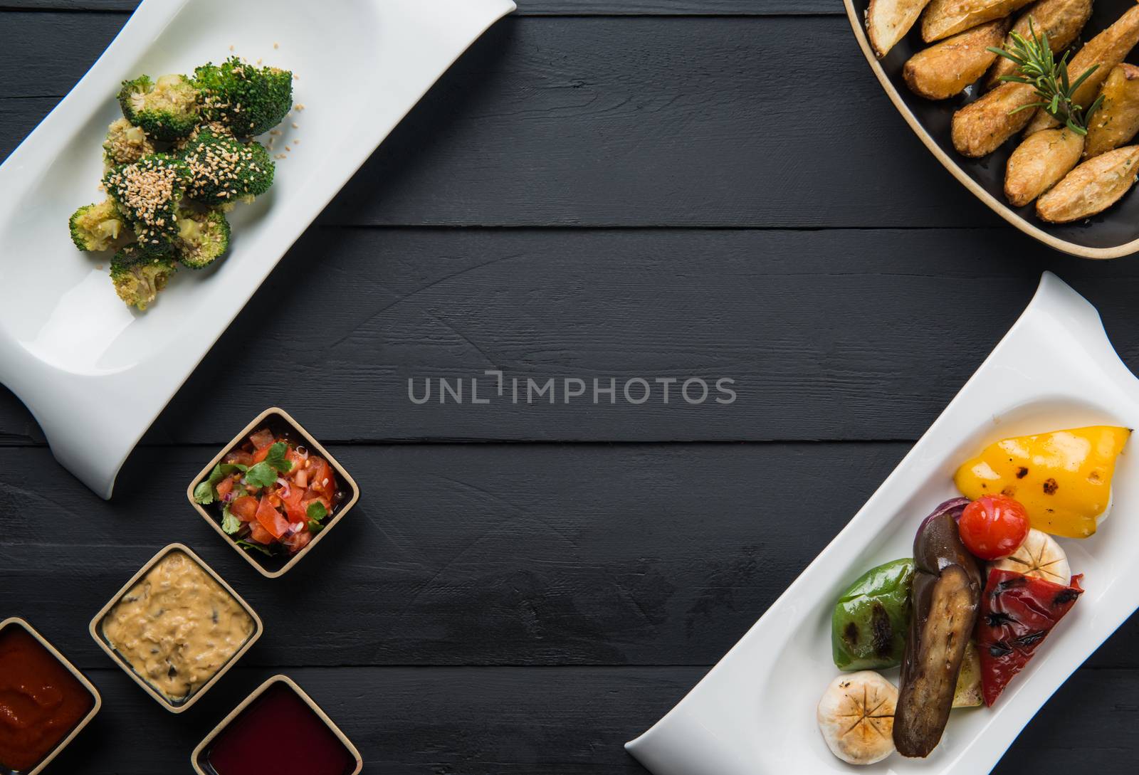 salads, vegetable food and gravy in plates on a black wooden background