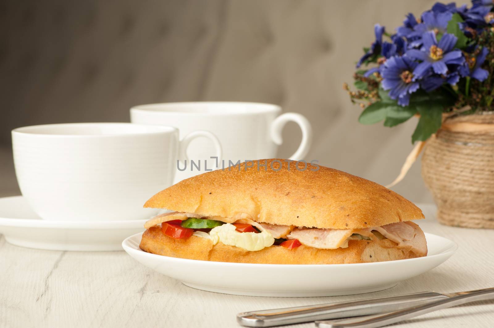 sandwich and two cups of coffee on a table with cutlery and flowers