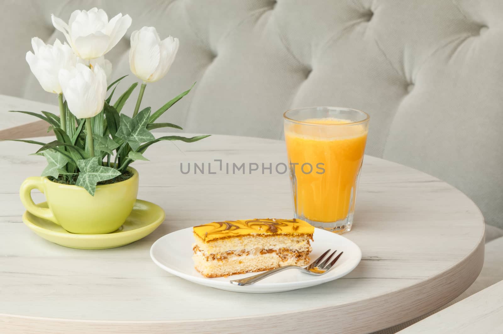 Cake and fork on a plate on a table with flowers on the background of the sofa