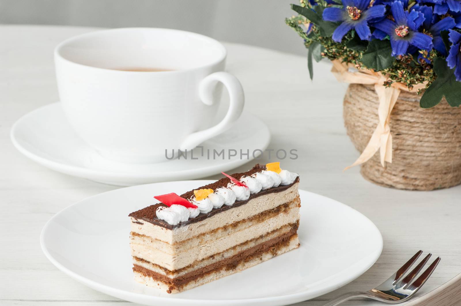 cake on a plate and a cup of coffee on a table with flowers