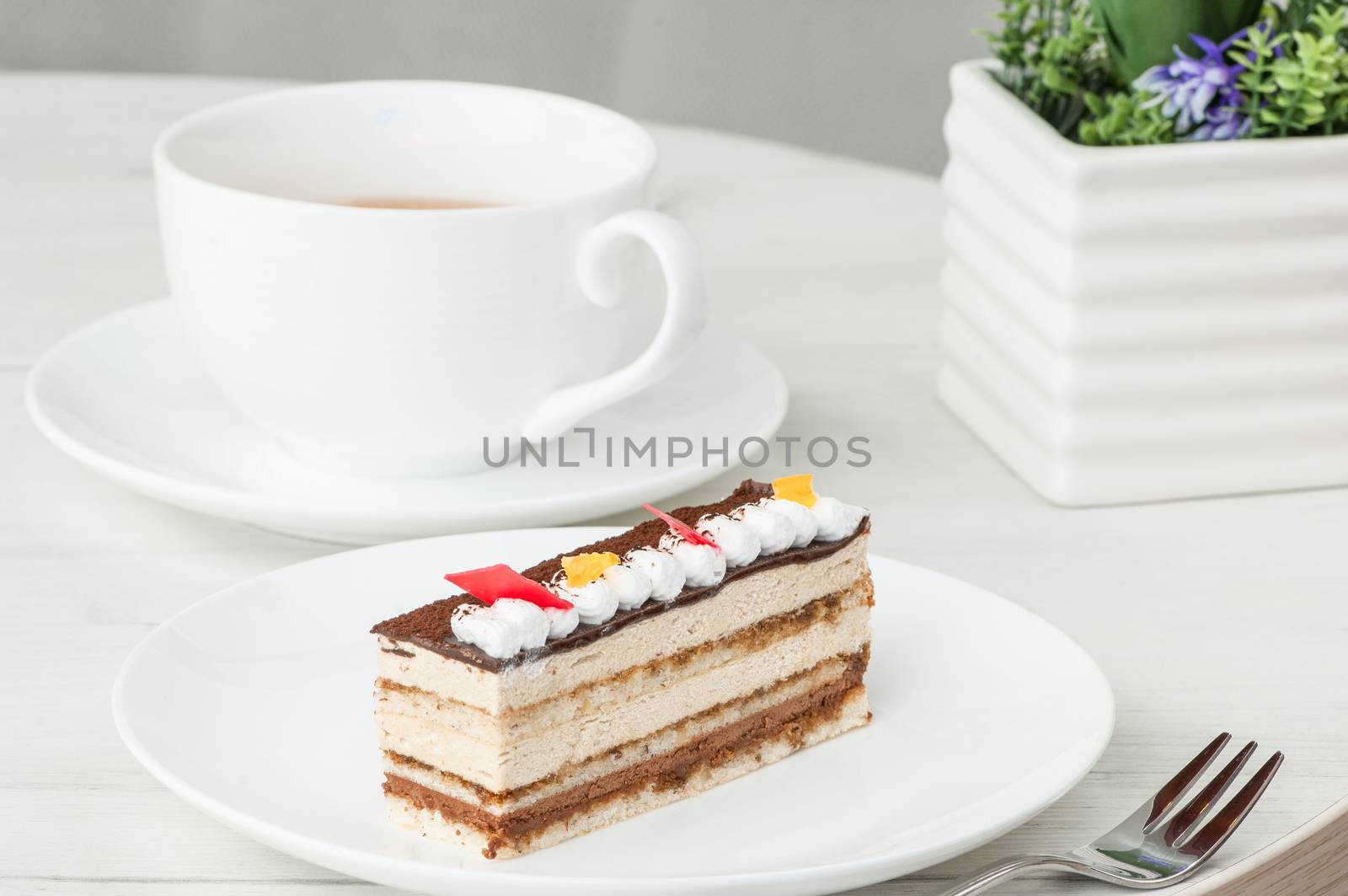 cake on a plate and a cup of coffee on a table with flowers