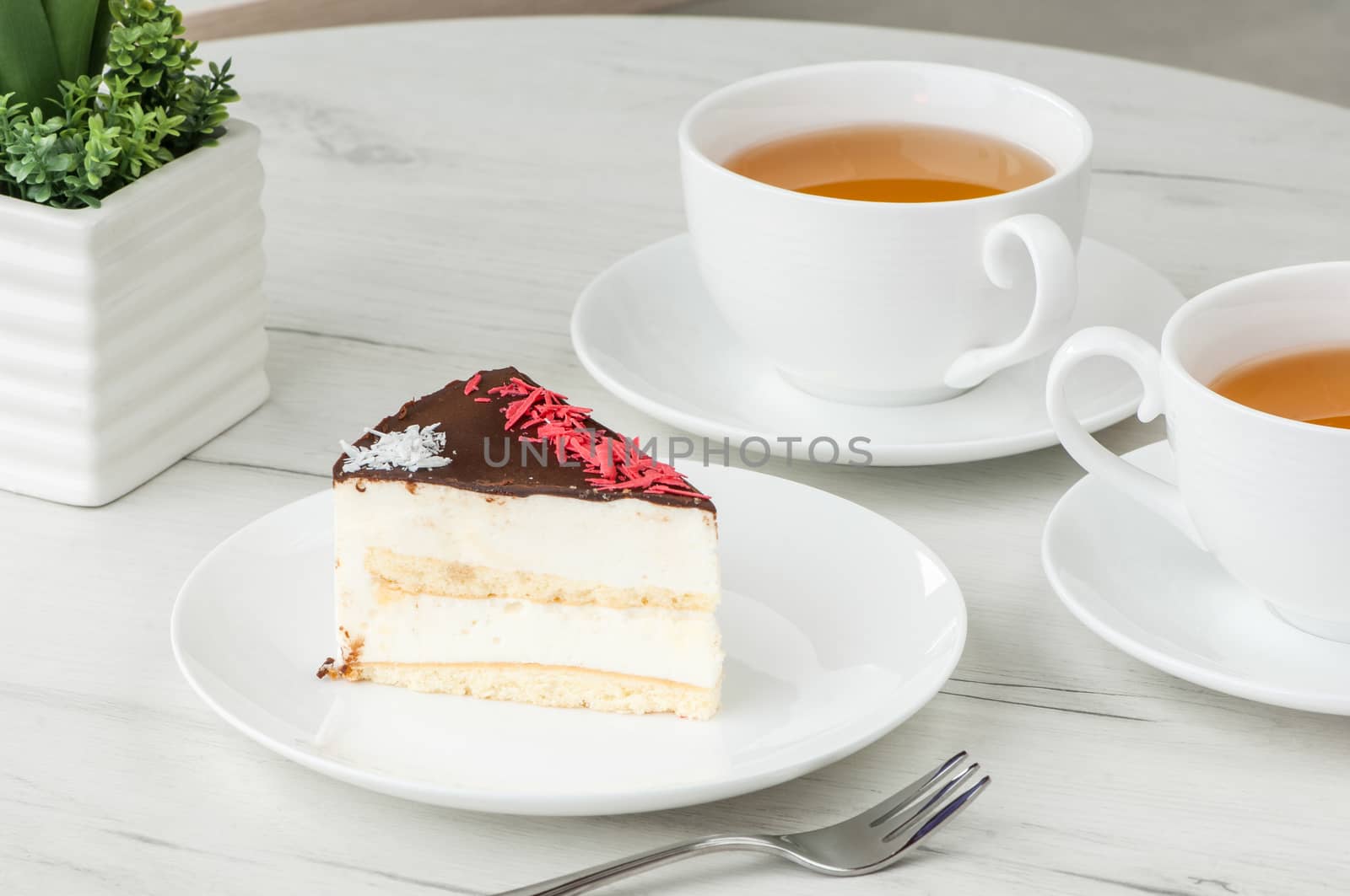 cake on a plate and two cups of tea on the table with flowers and a fork