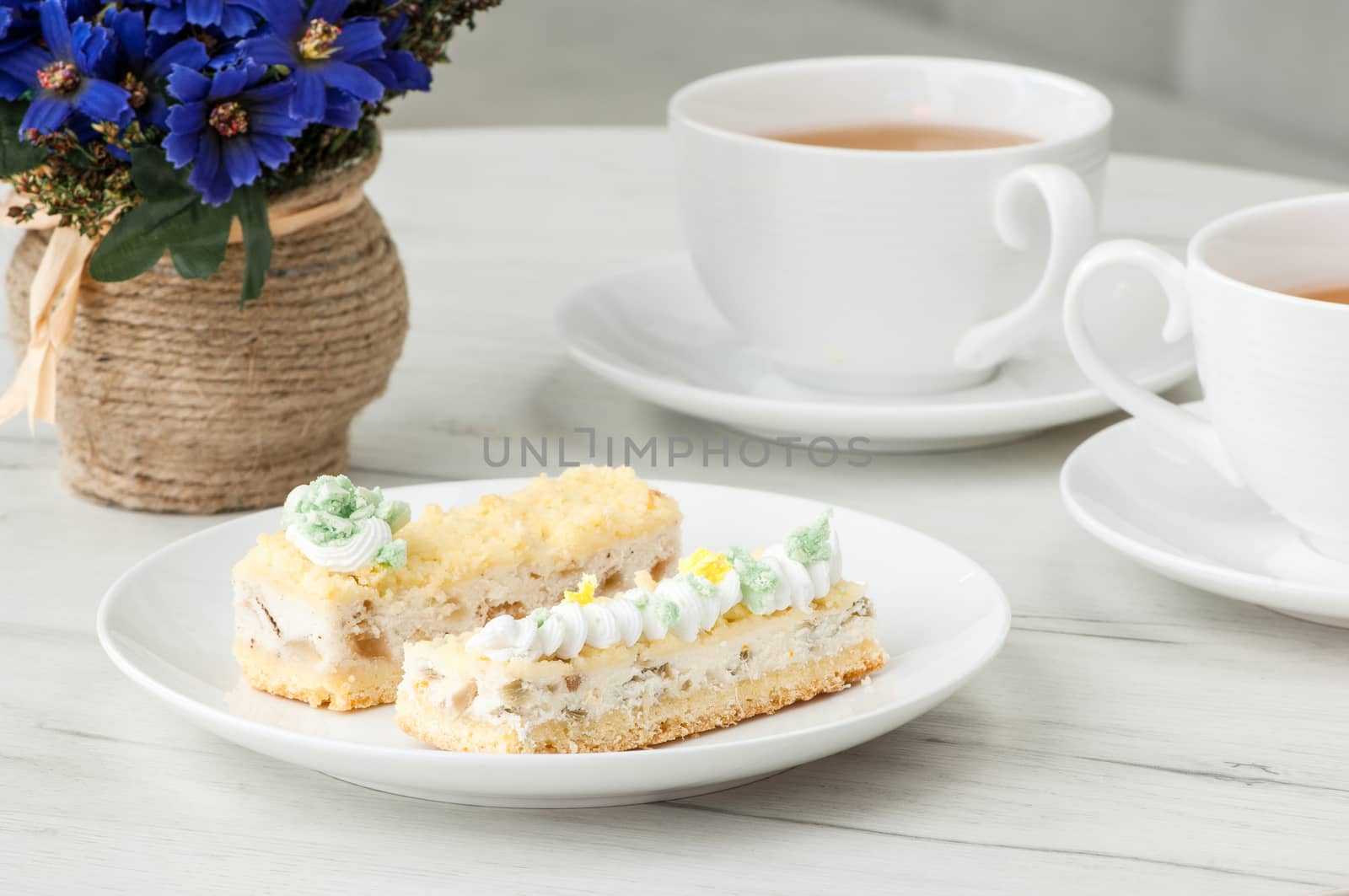 cake on a plate and two cups of tea on the table with flowers