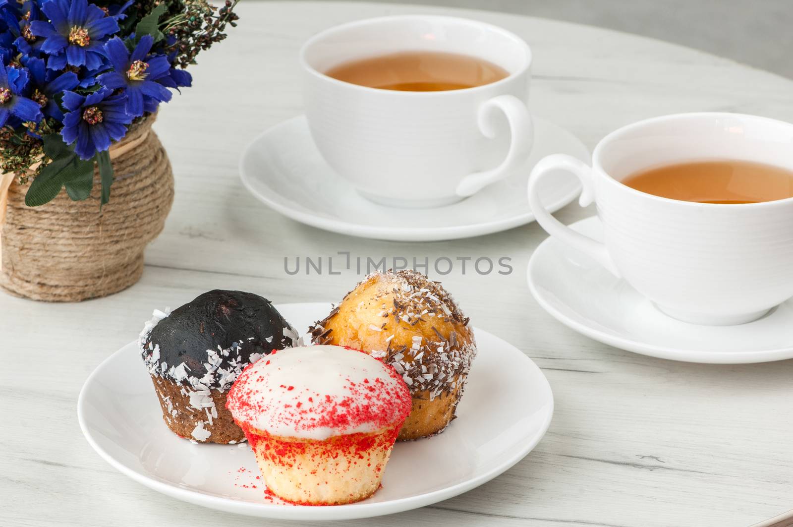 cake on a plate and two cups of tea on the table with flowers