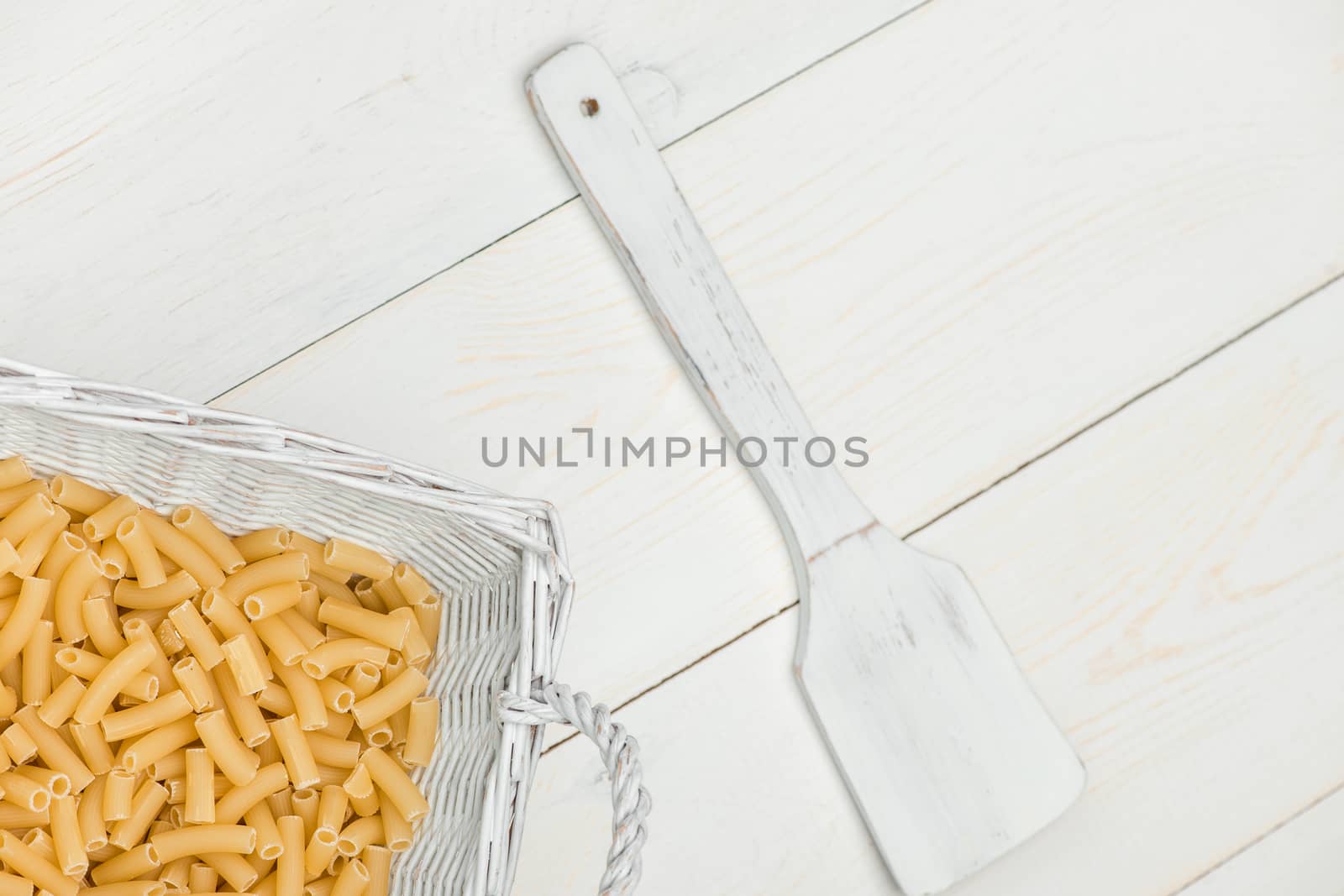 pasta in wicker basket and a wooden spoon on a white old wooden boards