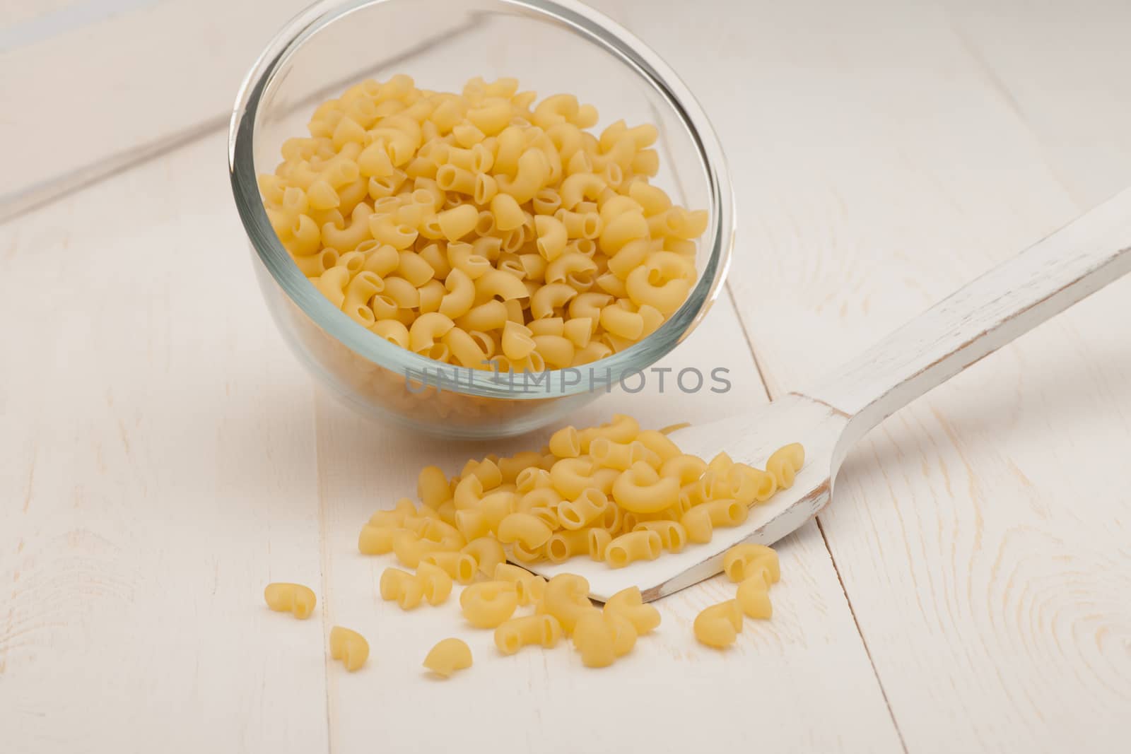 pasta in a transparent plate of glass and wooden spoon on a white old wooden boards