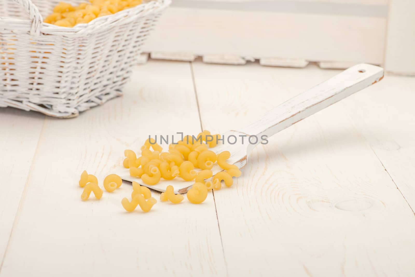 pasta in wicker basket and a wooden spoon on a white old wooden boards