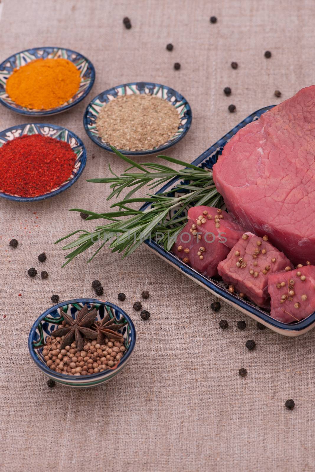raw meat with spices and herbs in a square plate on a textured tissue