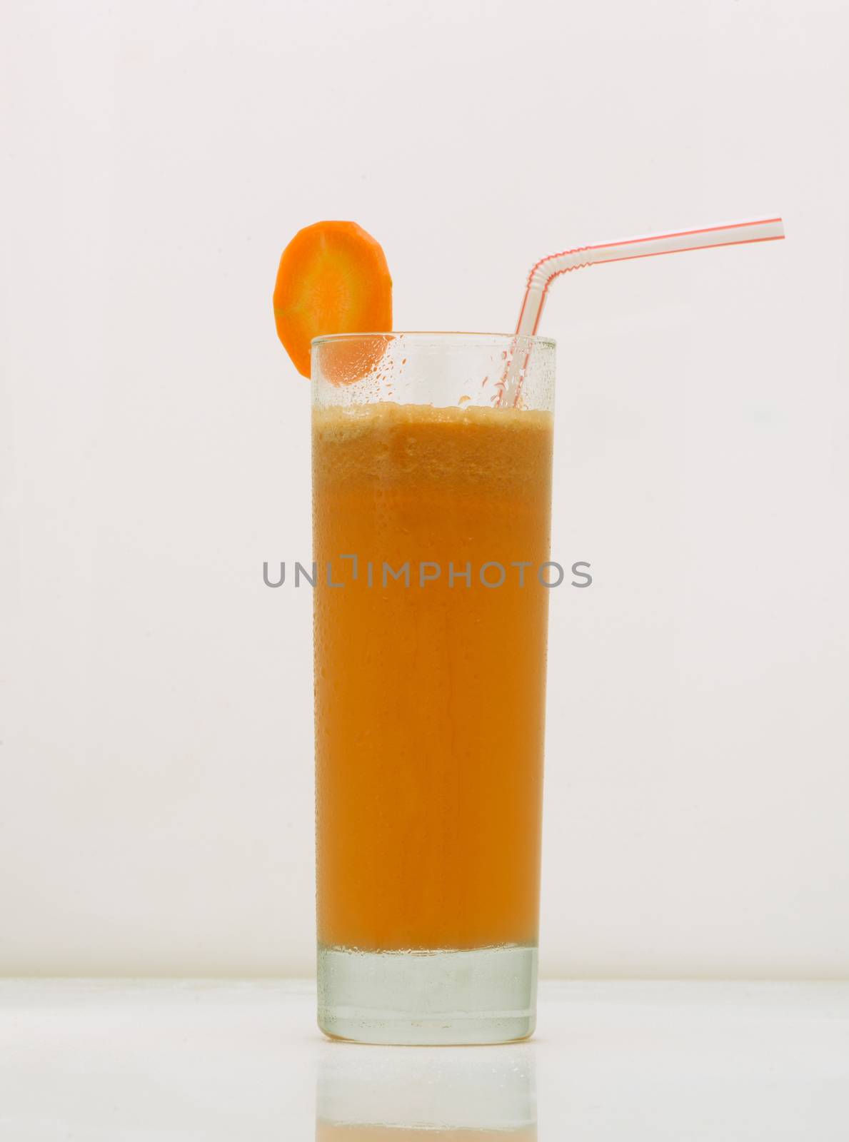 carrot juice in a glass with a straw and a slice of carrot. drink isolated on white background