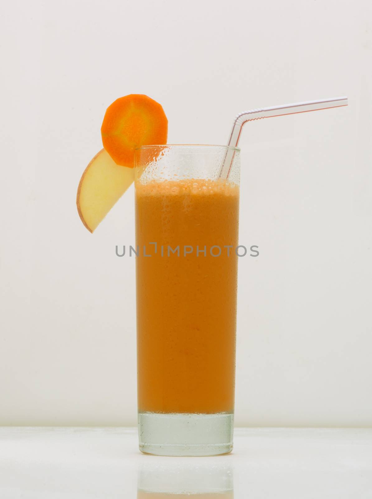 carrot juice in a glass with a straw and a slice of carrot and apple. drink isolated on white background
