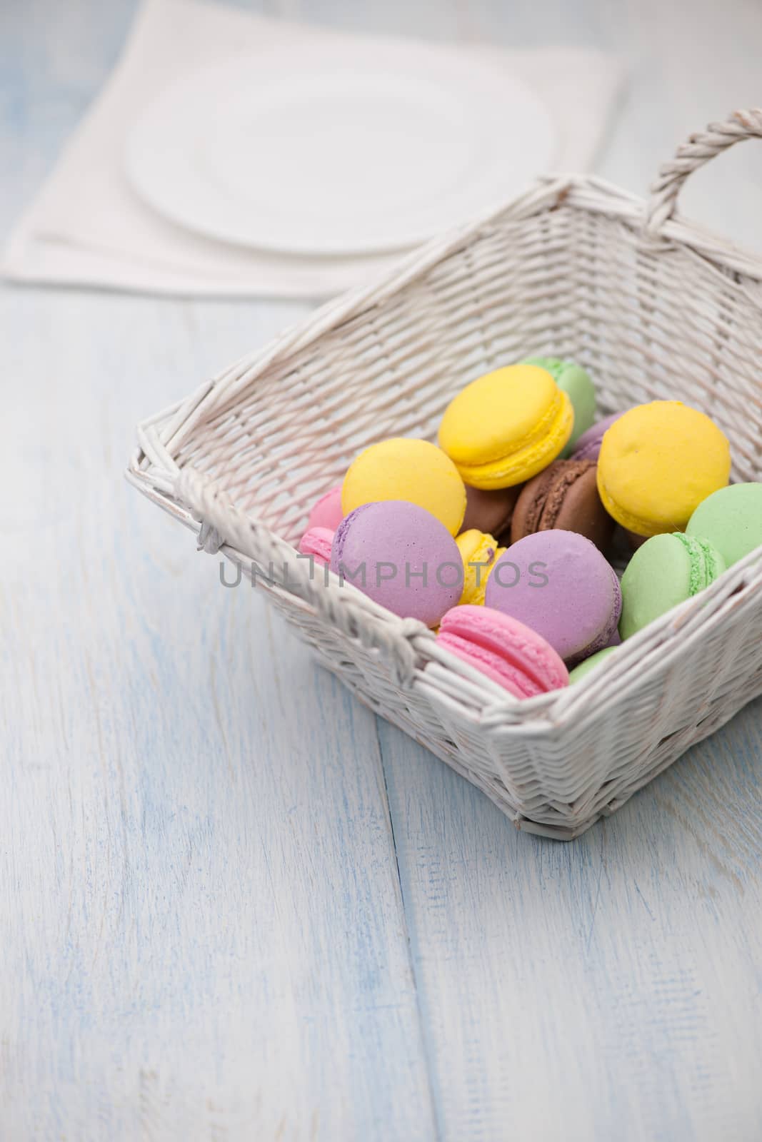 multi-colored circular cookies in a wicker basket and a plate on a napkin