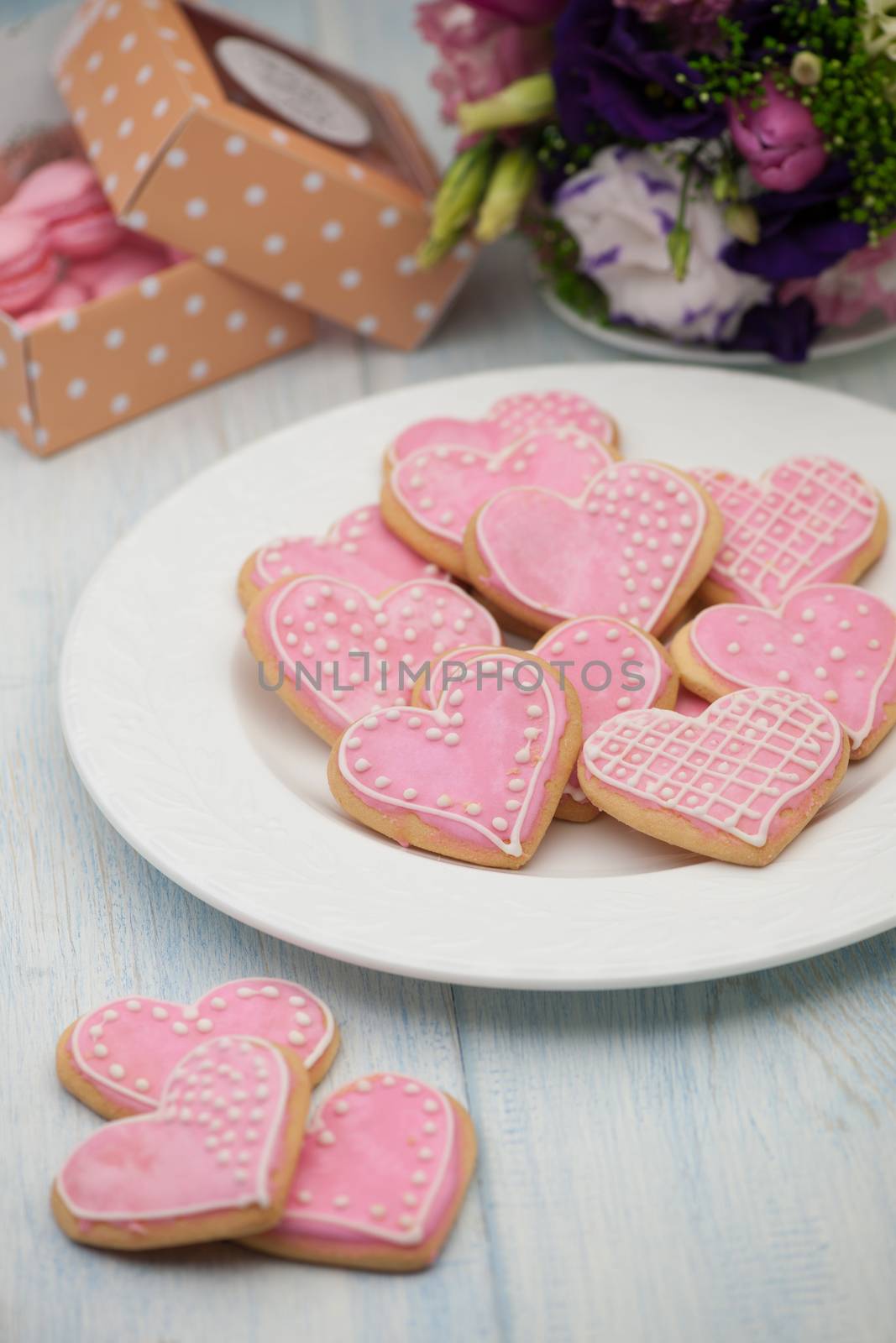 pink cookies in the shape of hearts on a plate and gift box and flowers on Valentine's Day