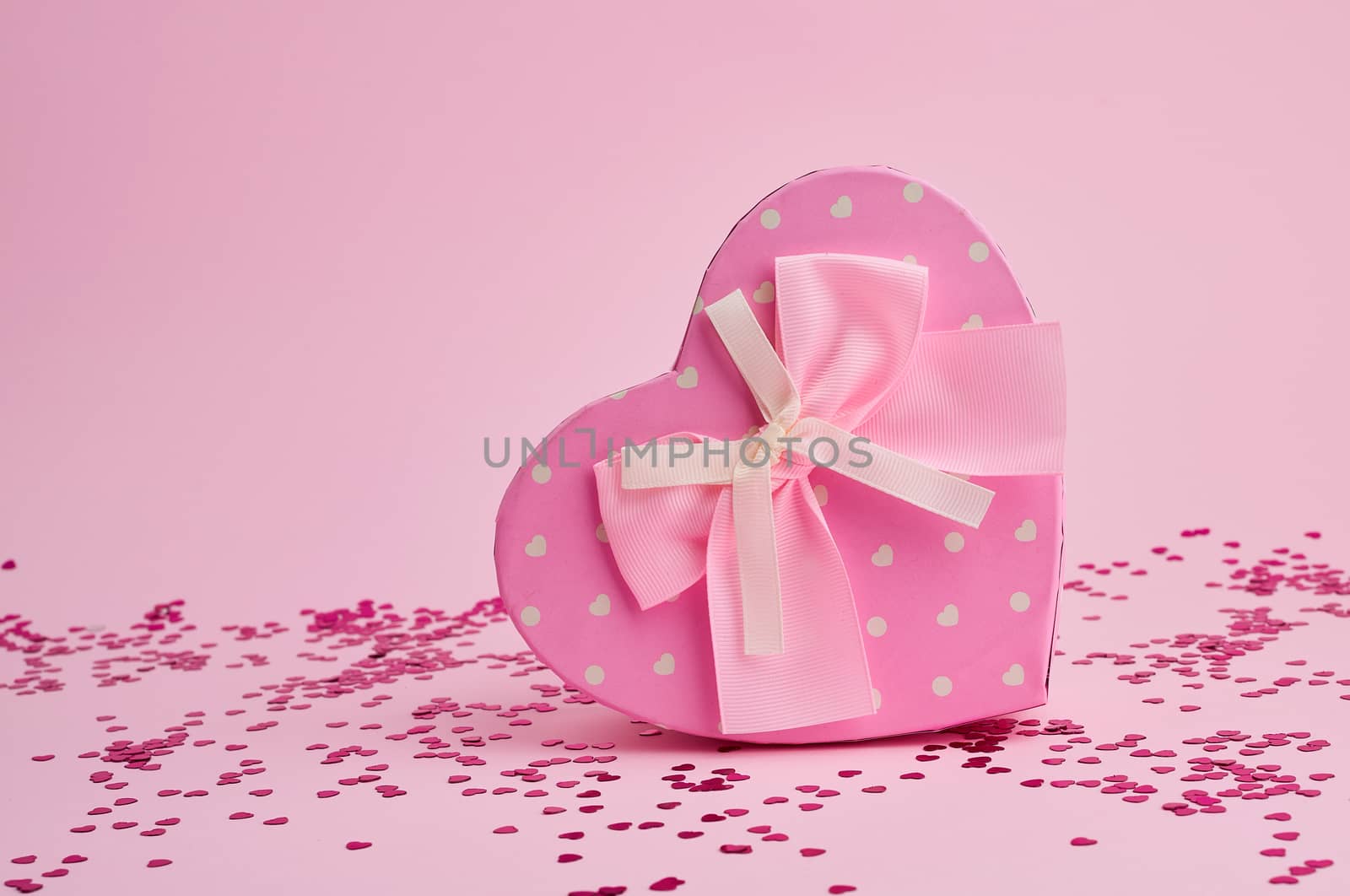 closed pink gift box in the form of a heart with a bow on a pink background, festive backdrop