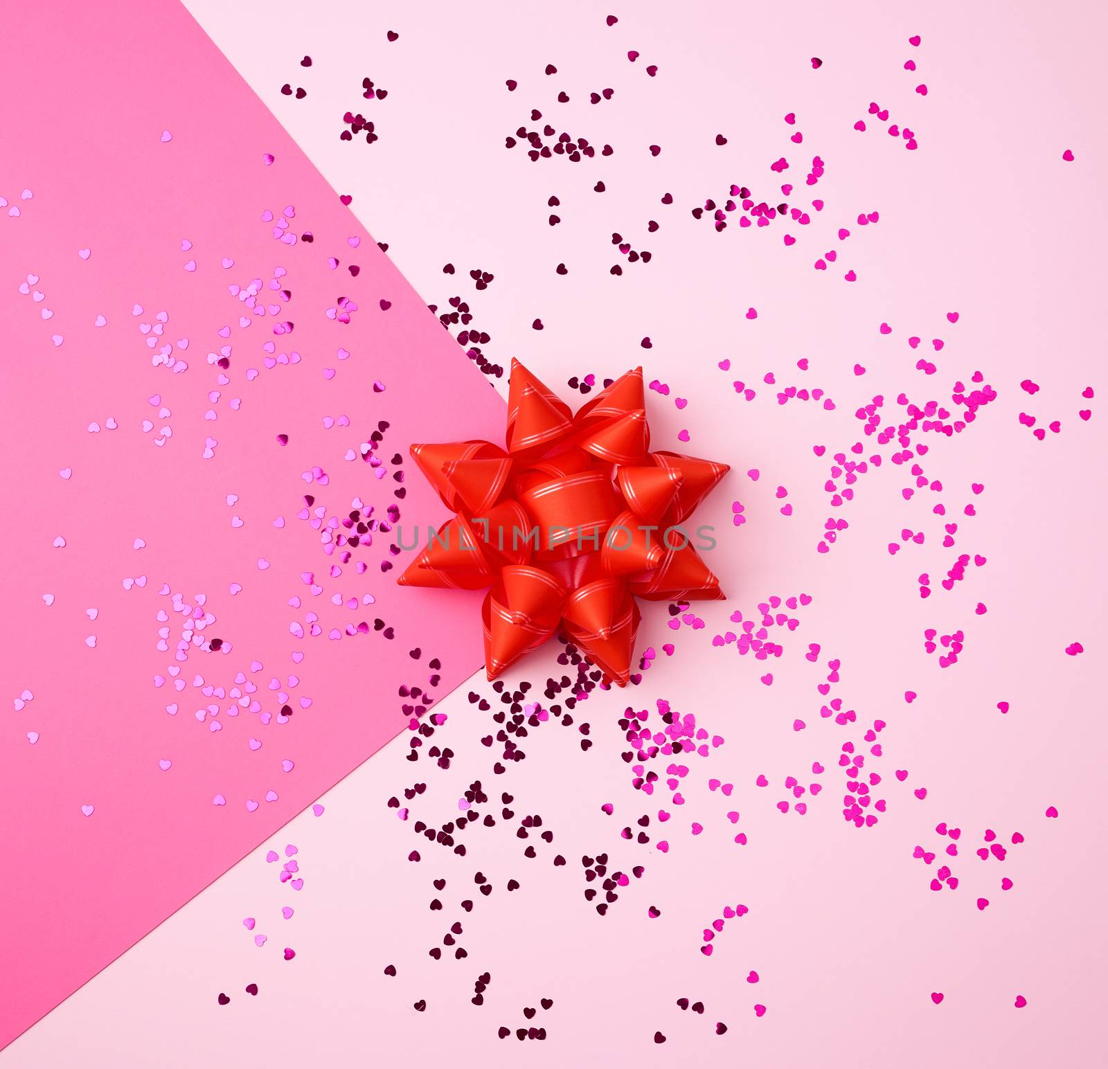 red bow and shiny multi-colored round confetti scattered on a pink background, festive backdrop for birthday, valentines day