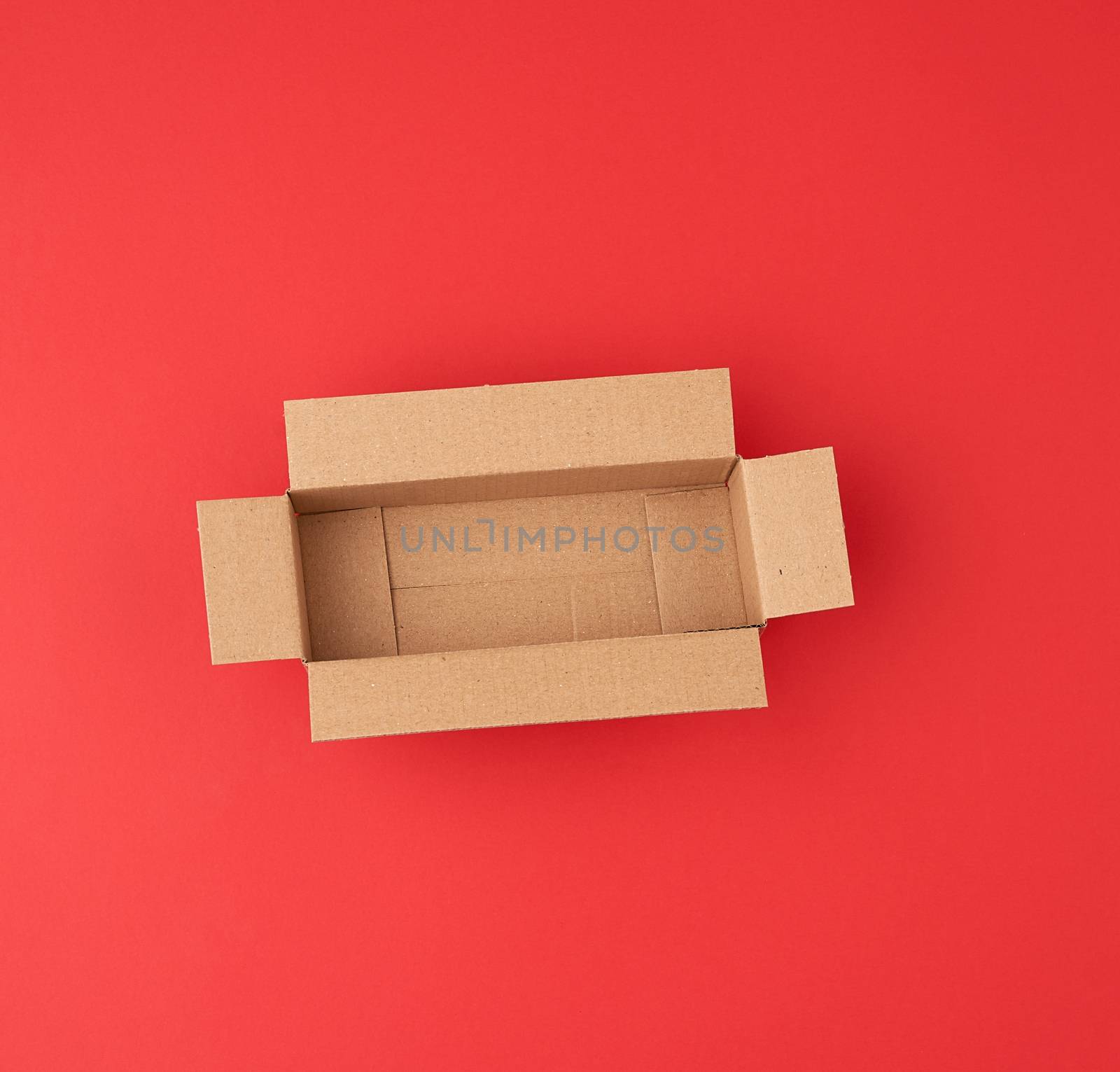 open empty square brown cardboard box for transportation and packaging of goods on red  background, top view.