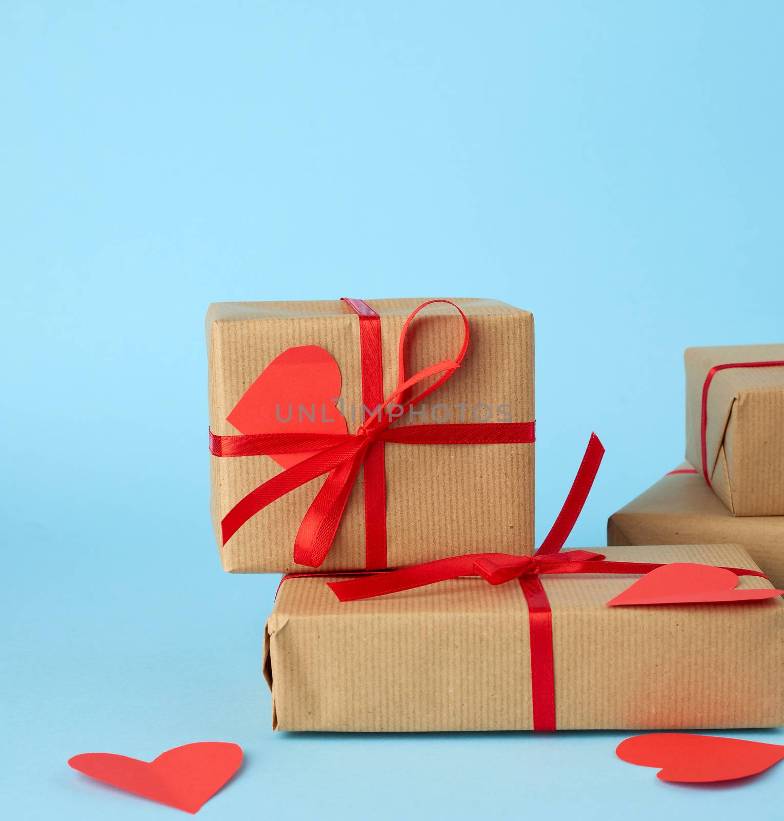 stack of wrapped gifts in brown kraft paper and tied with a red ribbon on a blue background, surprise and a gift for Valentine's Day February 14