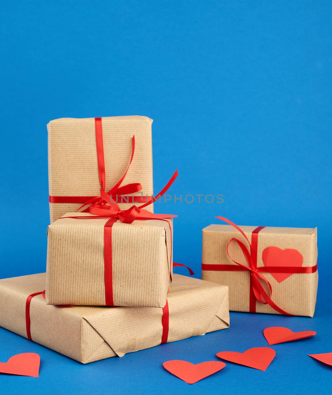 stack of wrapped gifts in brown kraft paper and tied with a red ribbon on a blue background, surprise and a gift for Valentine's Day February 14