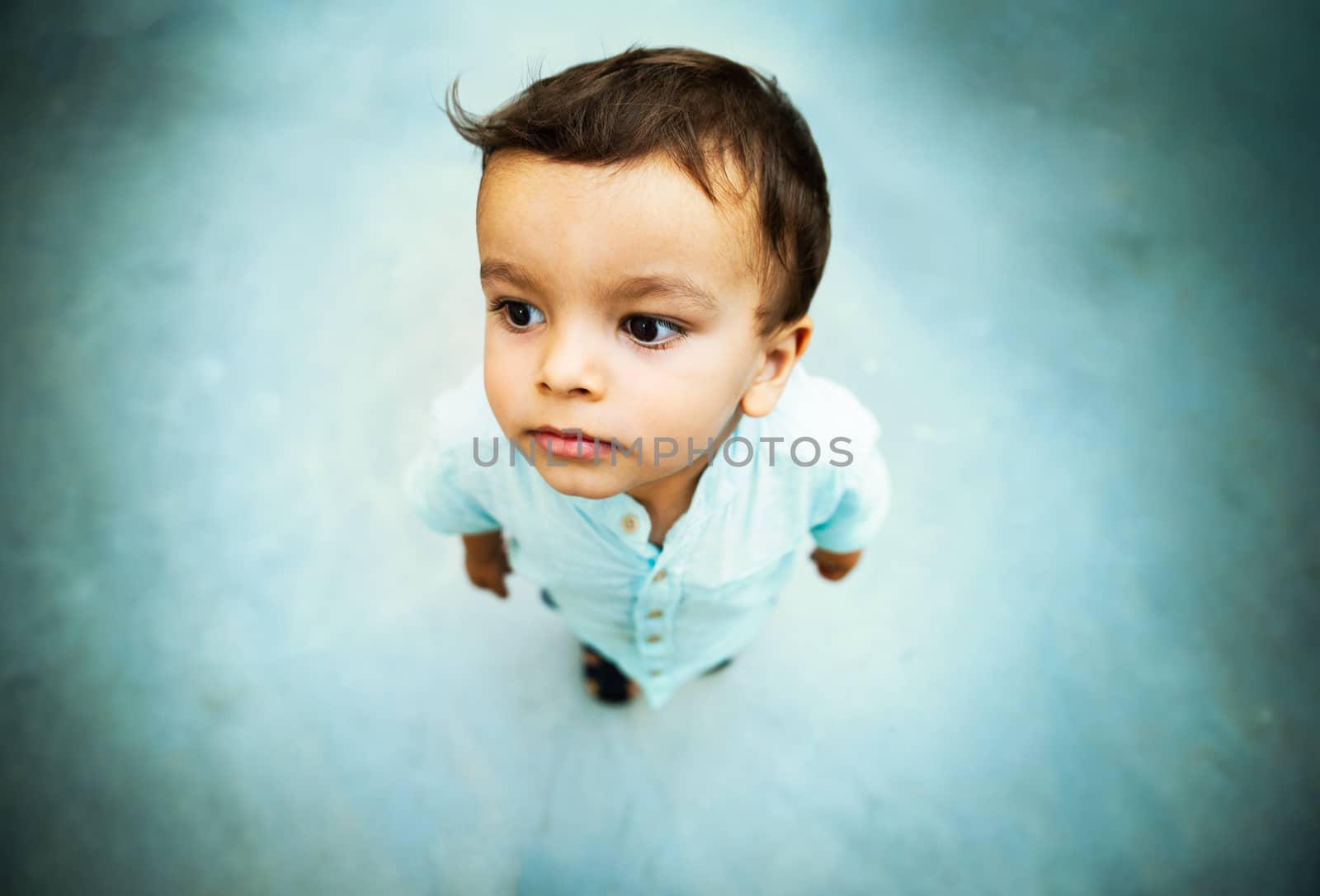 Little boy high angle shot portrait with shallow depth of field, grungy blue tone concrete floor background and vignette.