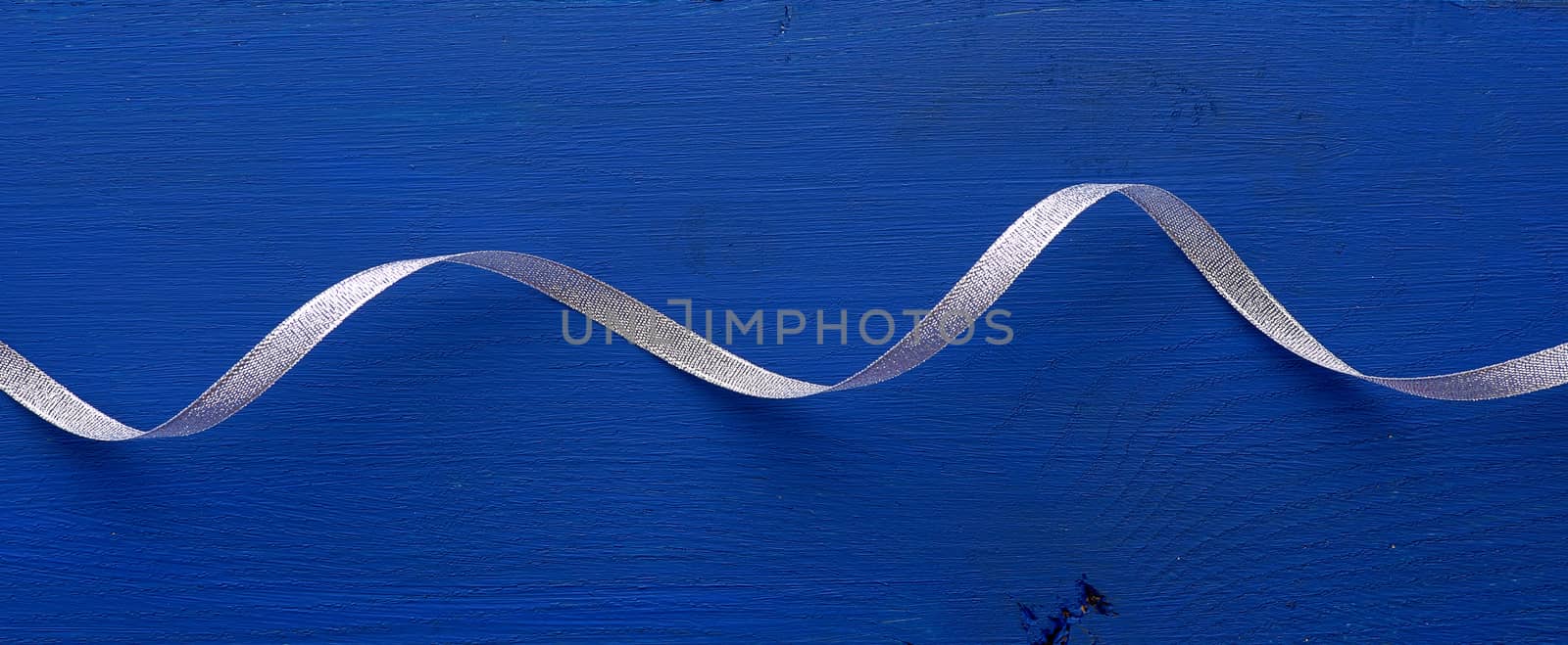 gray shiny thin ribbon twisted on a blue wooden background, trendy classic color, close up