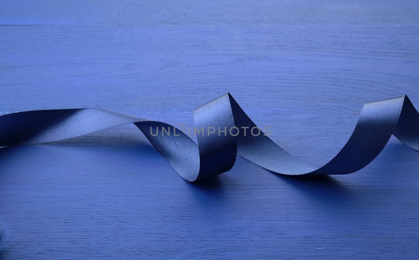 blue silk thin ribbon twisted on a blue wooden background, trendy classic color, close up