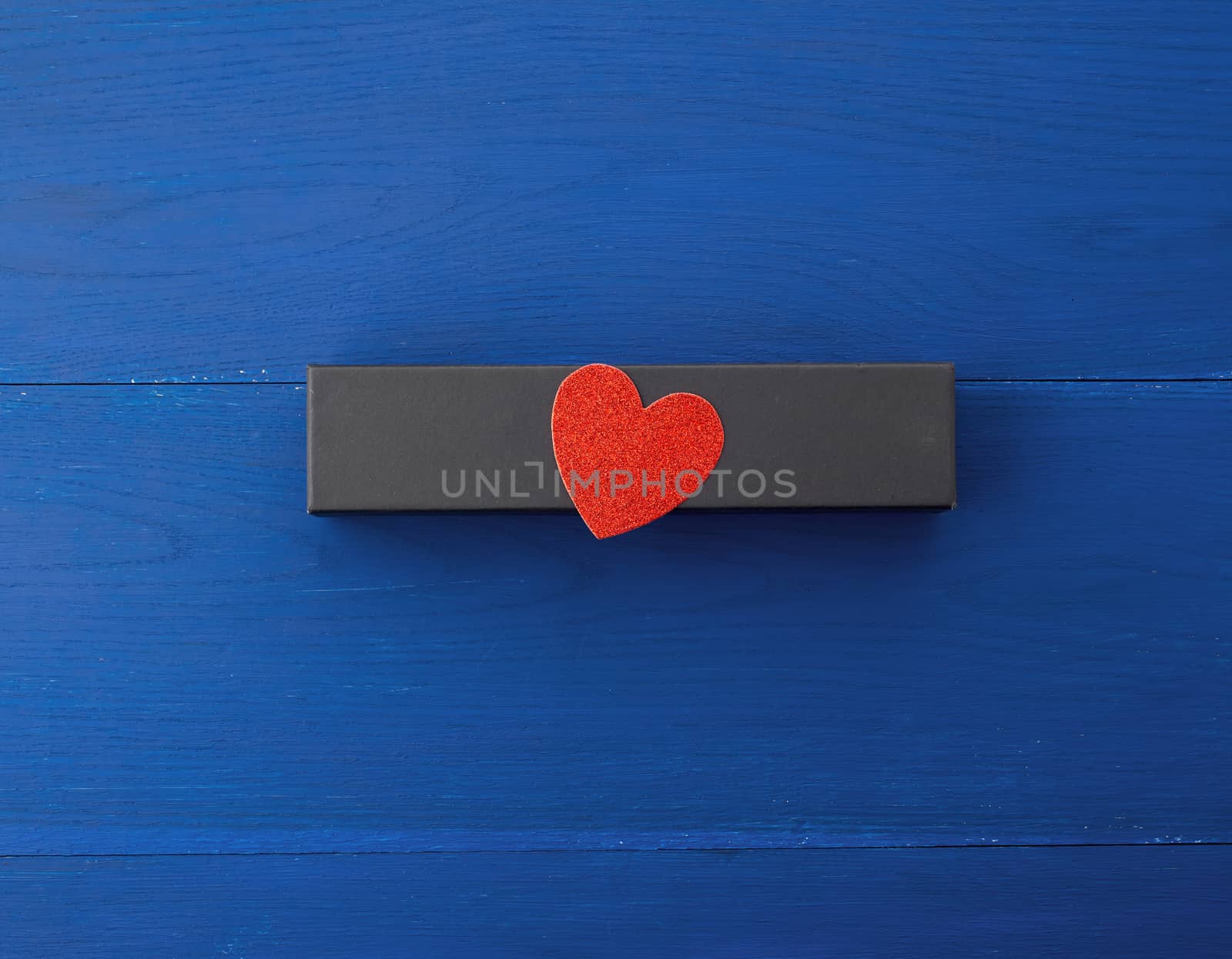 closed rectangular cardboard box with a gift, red paper heart from above, blue wooden background from boards, top view