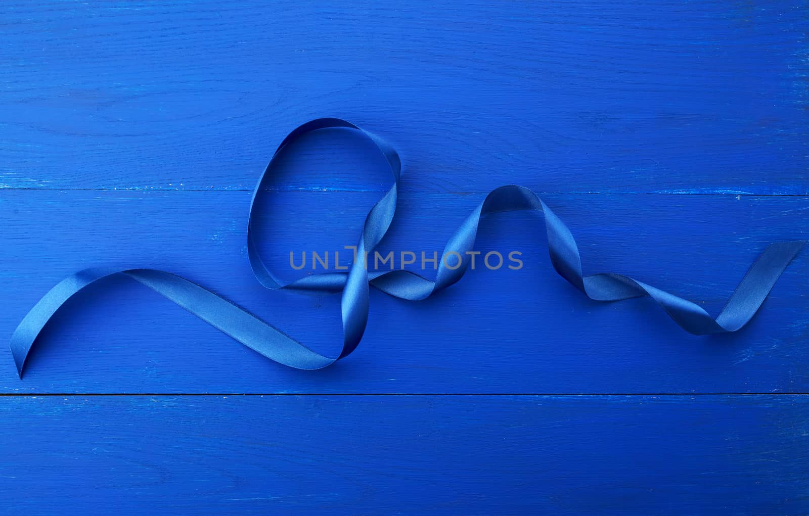 twisted silk blue ribbon on a blue wooden background, abstract holiday backdrop