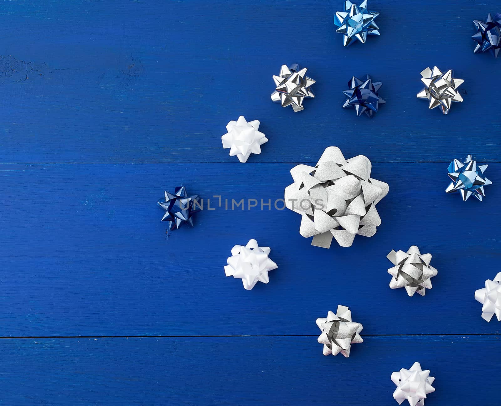 related white, blue and gray bows for gifts on a blue wooden background, decor for decorating gifts, top view