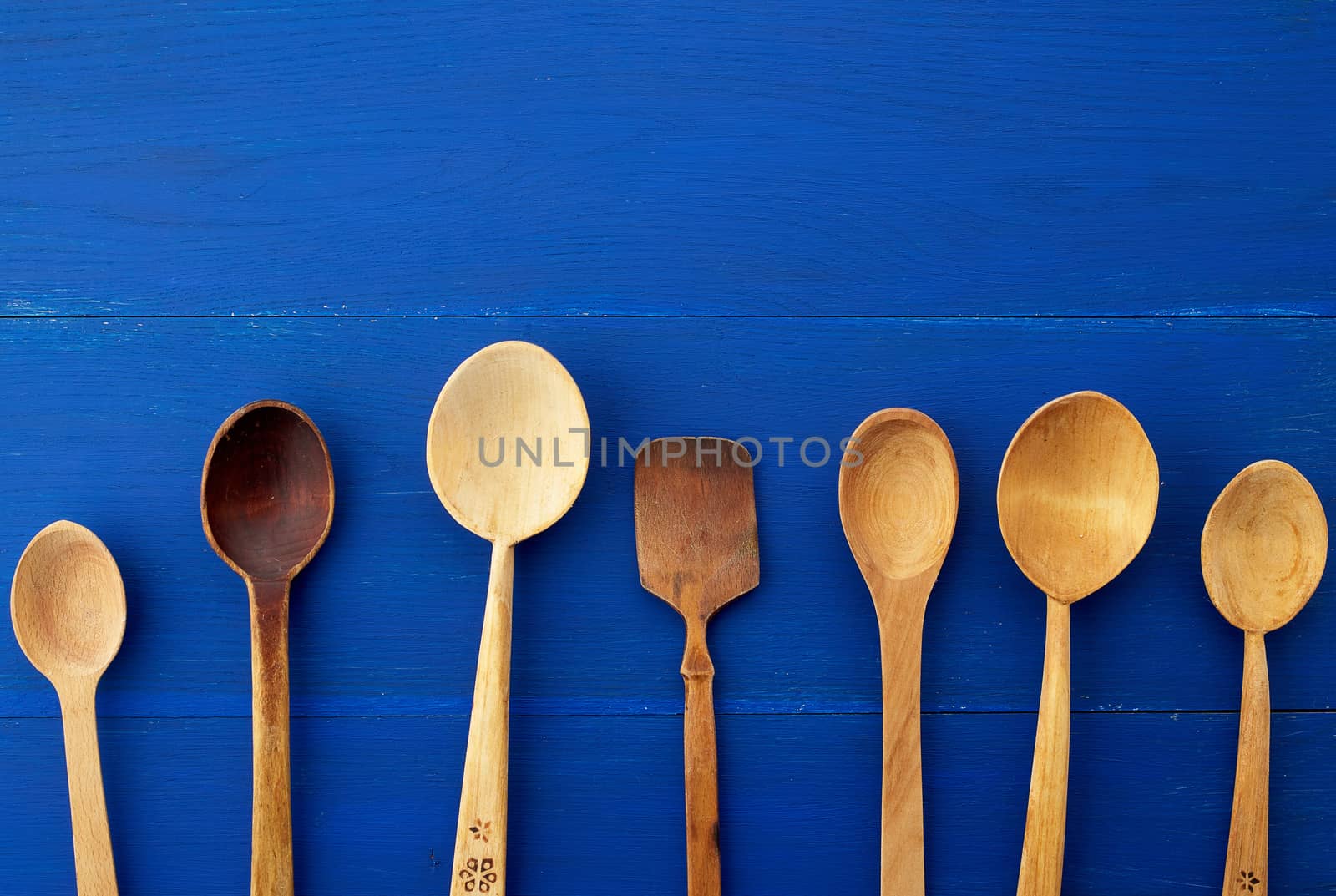 set of yellow wooden vintage spoons on a blue wooden background, top view, copy space. Household equipment. Kitchen utensil. 