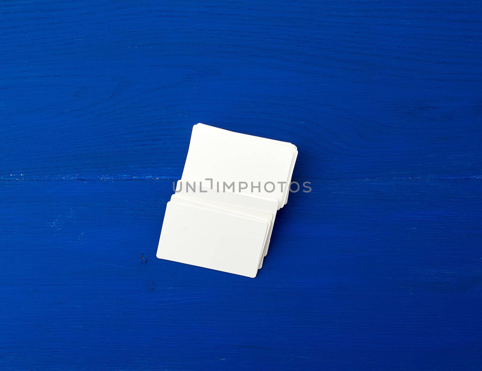 stack of white blank paper rectangular business cards on blue wooden background, template for designer