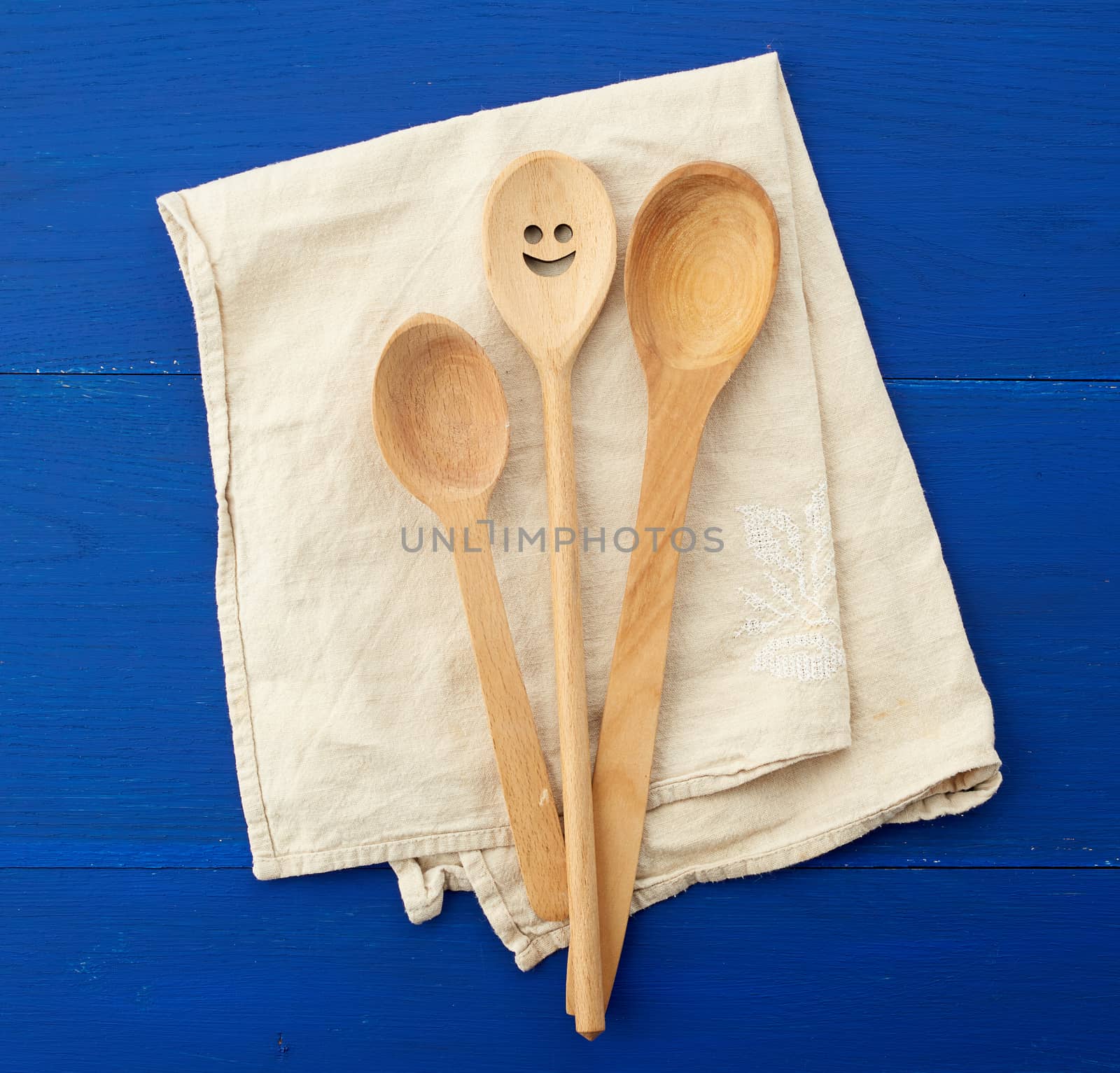 vintage wooden spoons and white textile kitchen towel on blue wooden background, top view