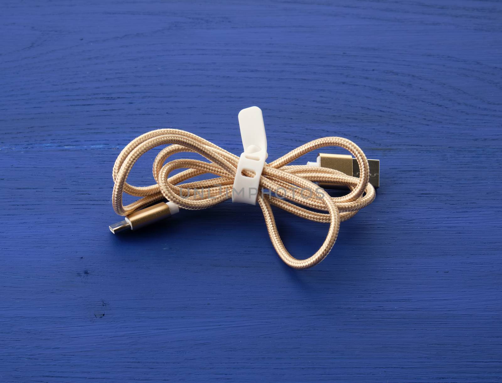 twisted golden cable for charging with electricity equipment in textile winding on a blue wooden background, close up