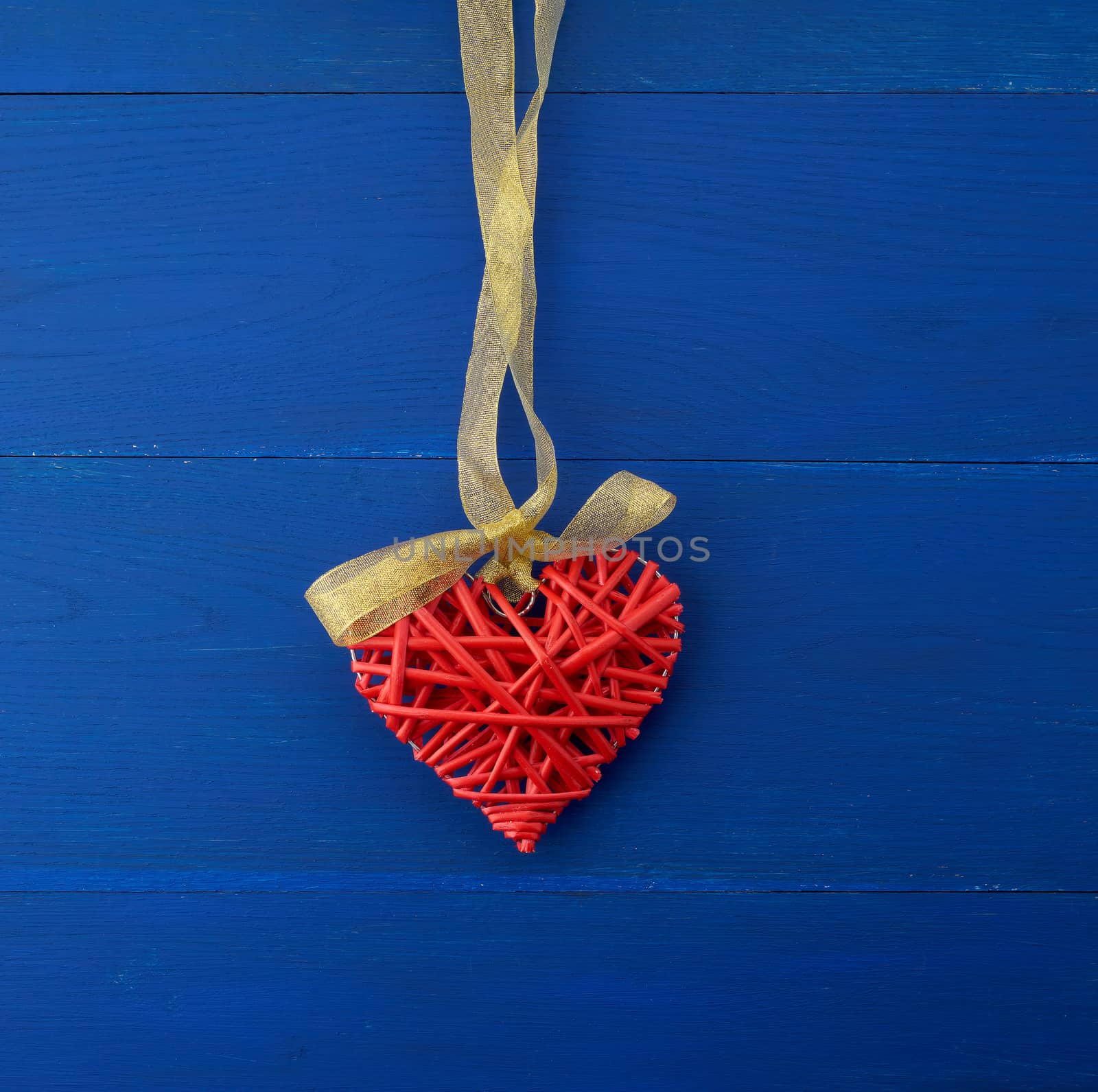 red wicker decorative heart hanging on silk golden ribbon, blue wooden festive background for Valentine's day