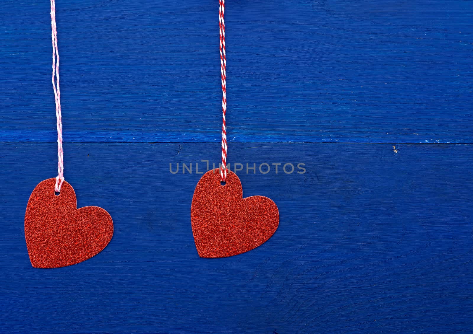 paper red shiny decorative hearts hanging on a rope on a dark blue wooden background, abstract holiday backdrop for valentines day on february 14