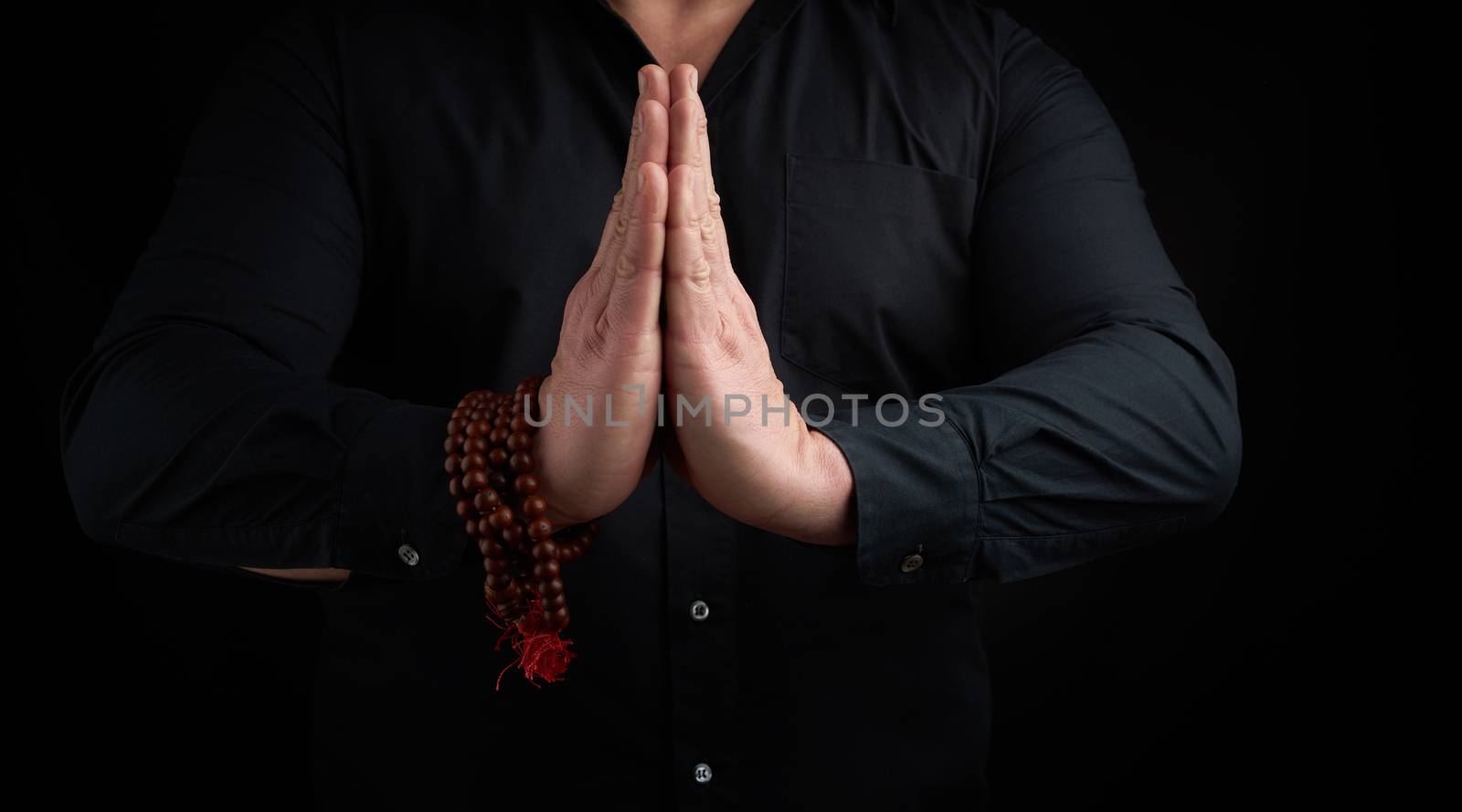 Two male hands joined before the breast, man in black shirt shows Namaste prayer mudra