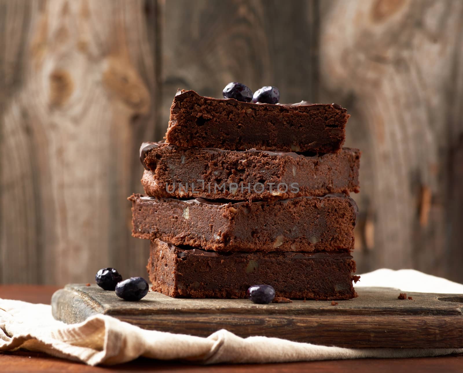 stack of square baked slices of brownie chocolate cake with walnuts on a wooden surface. Cooked homemade food. Chocolate pastry. Sweet meal, homemade dessert. Wooden table.